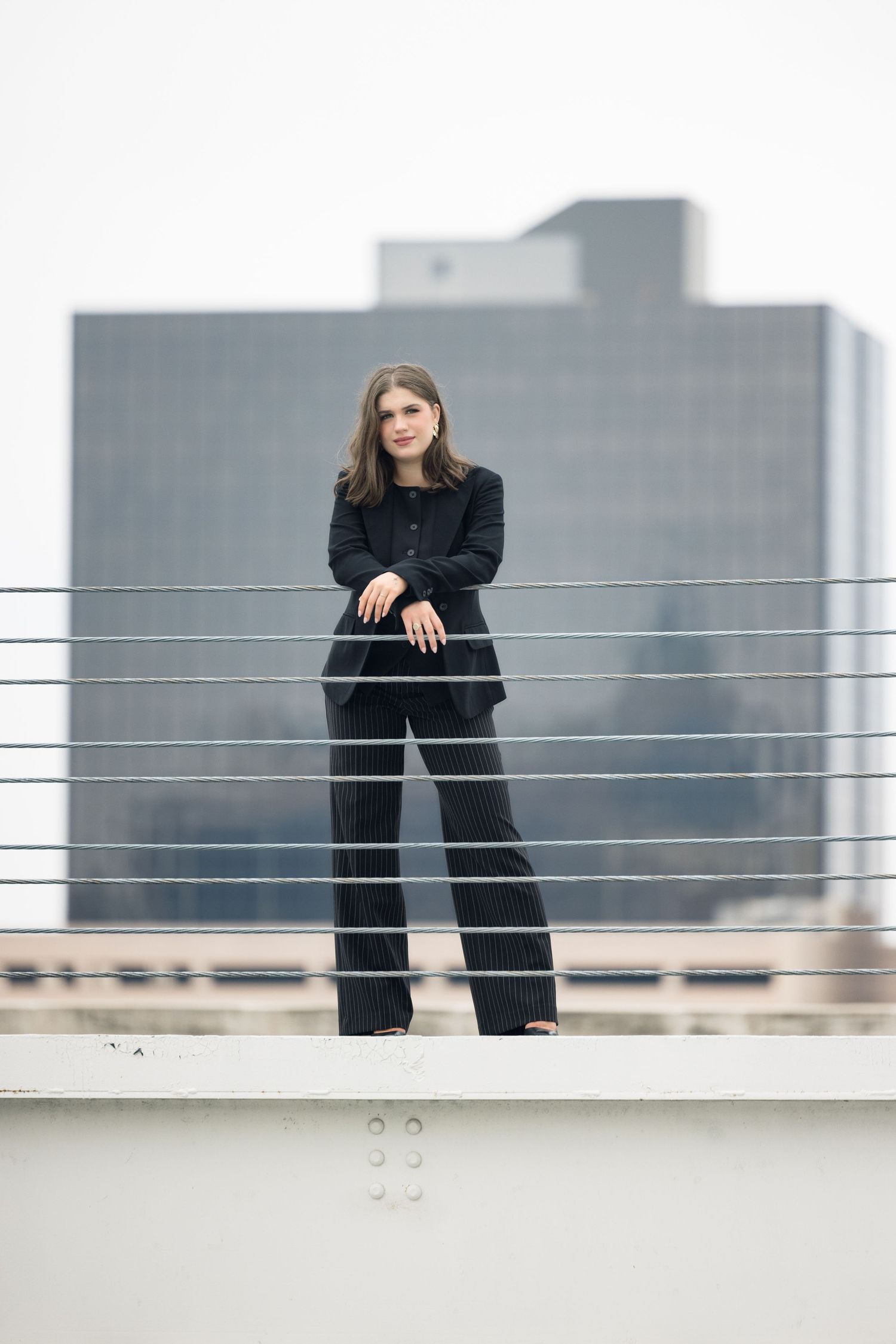 Rooftop photoshoot with modern railing and cityscape backdrop.