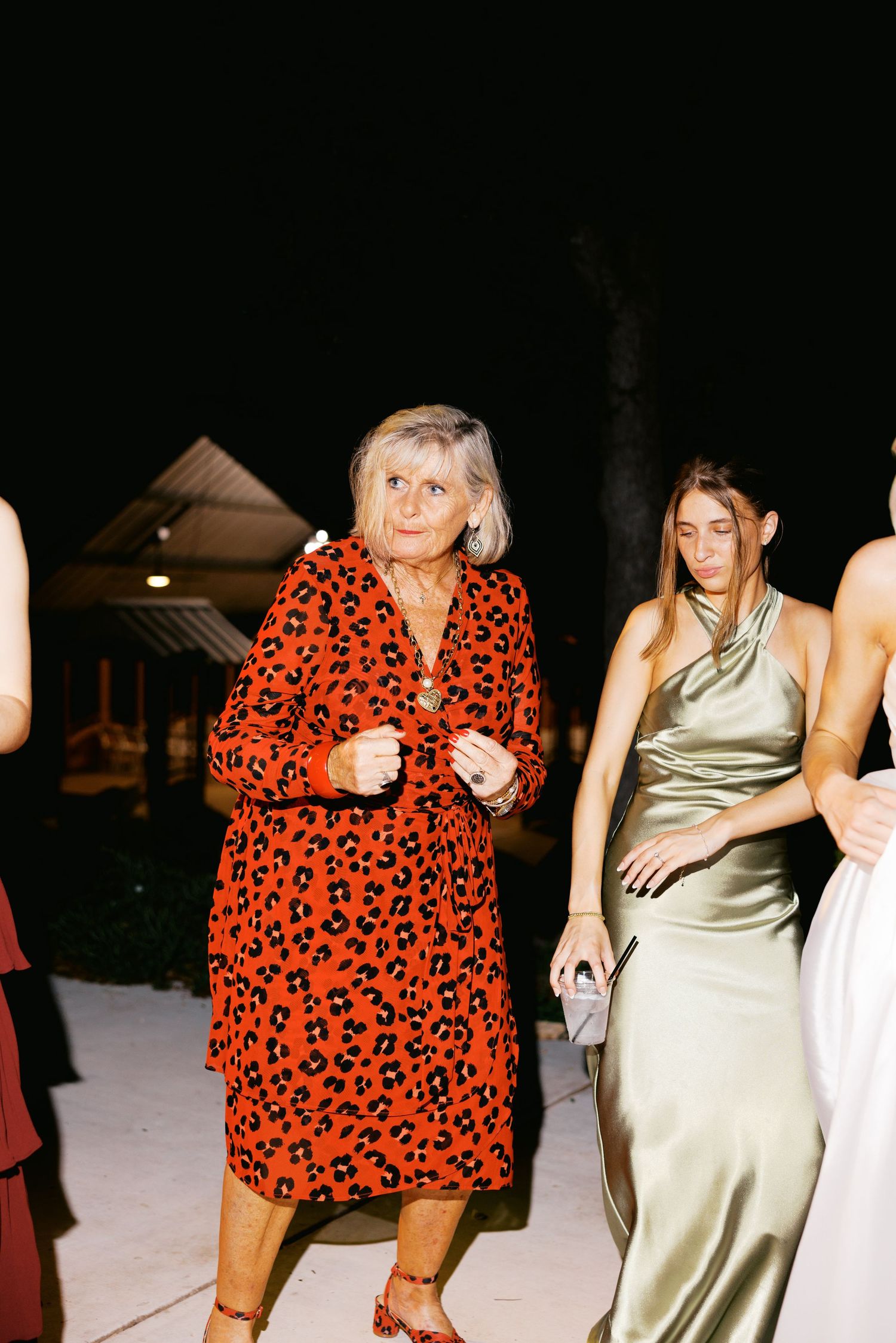 Elderly woman in red leopard print dress dancing at an outdoor evening wedding reception.