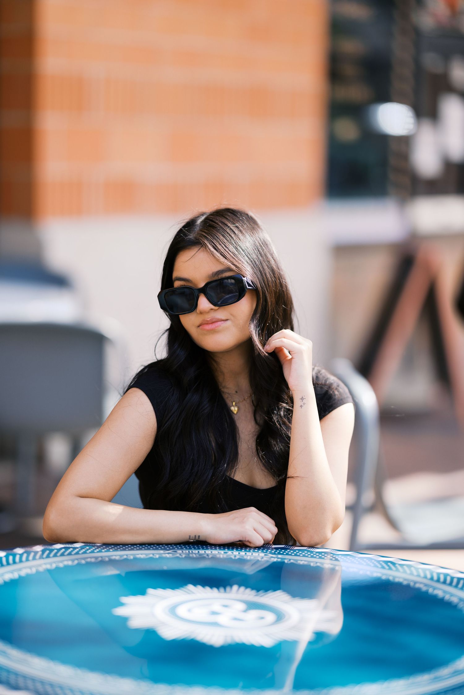 Casual portrait at outdoor cafe table with blue umbrella wearing sunglasses and black top.