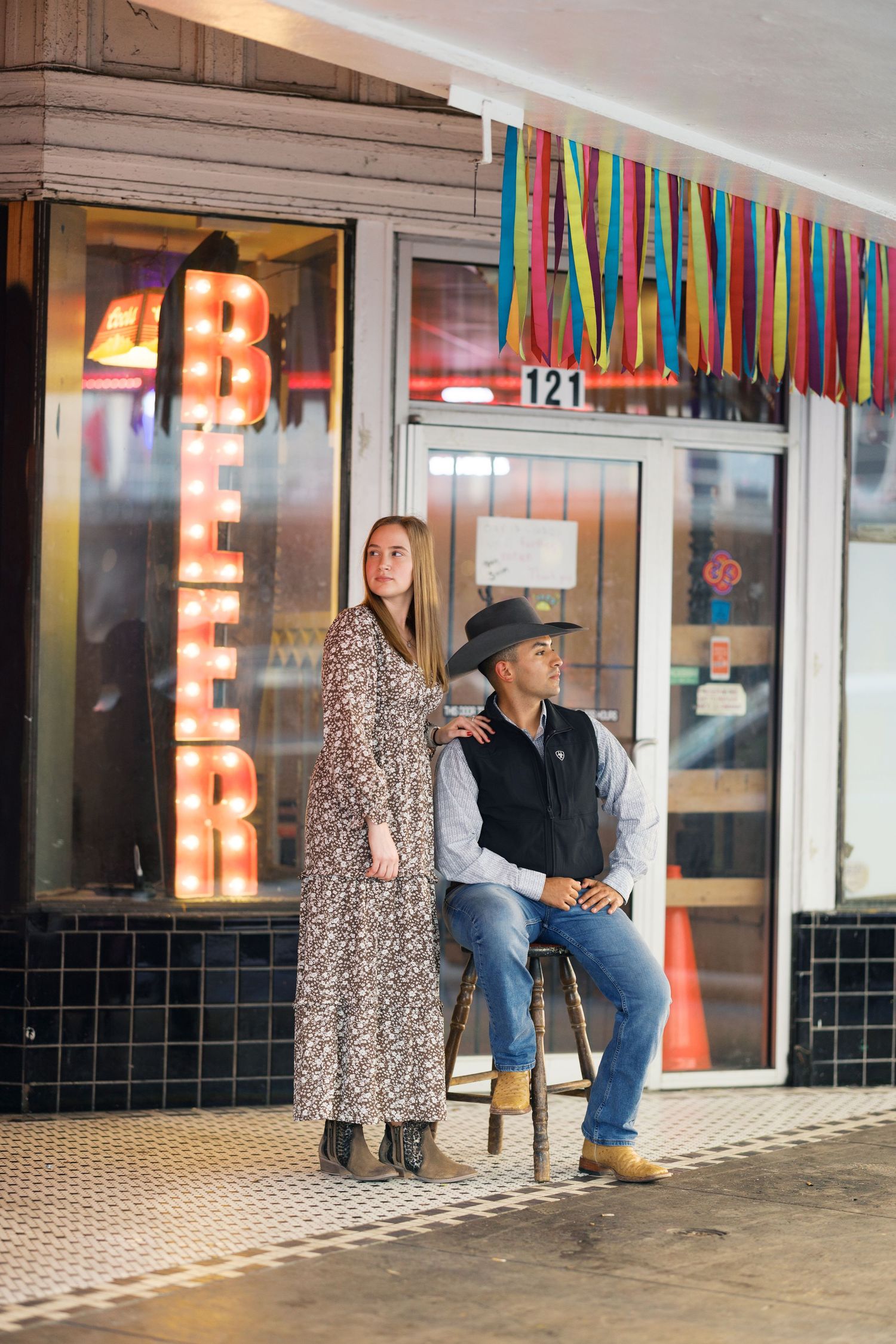 A couple standing together outside a storefront with festive decorations and neon lighting.