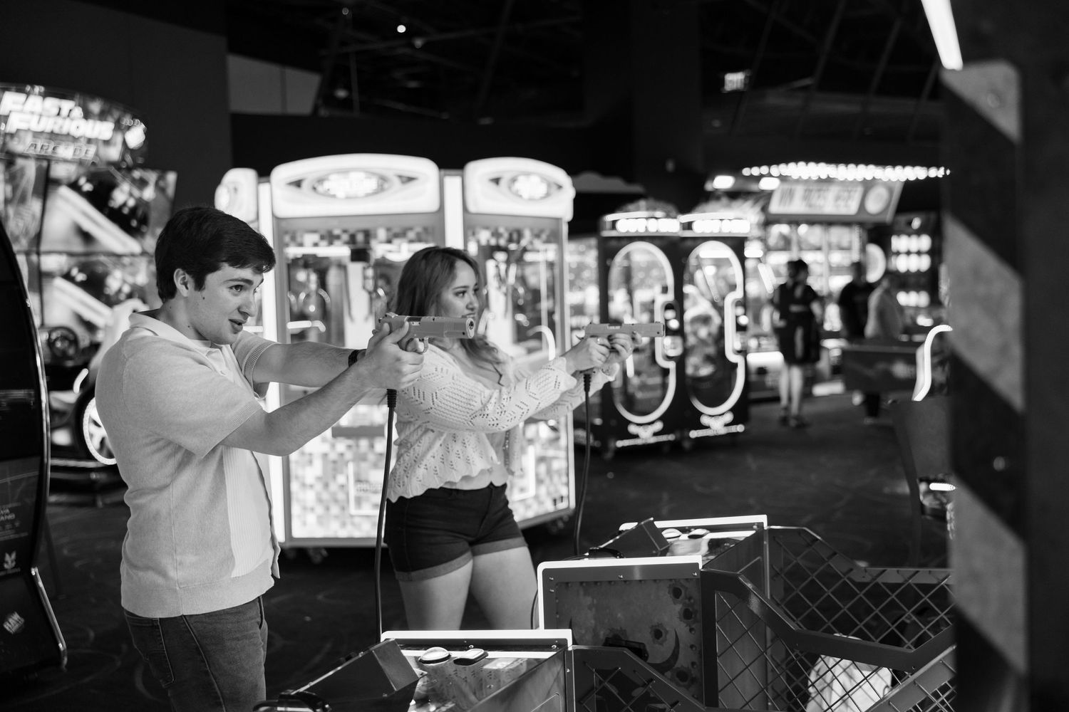 People playing arcade games in black and white with neon signs glowing.