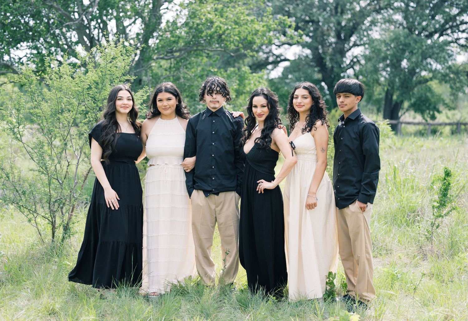 Group photo of people wearing black and beige outfits standing together in a natural outdoor setting.