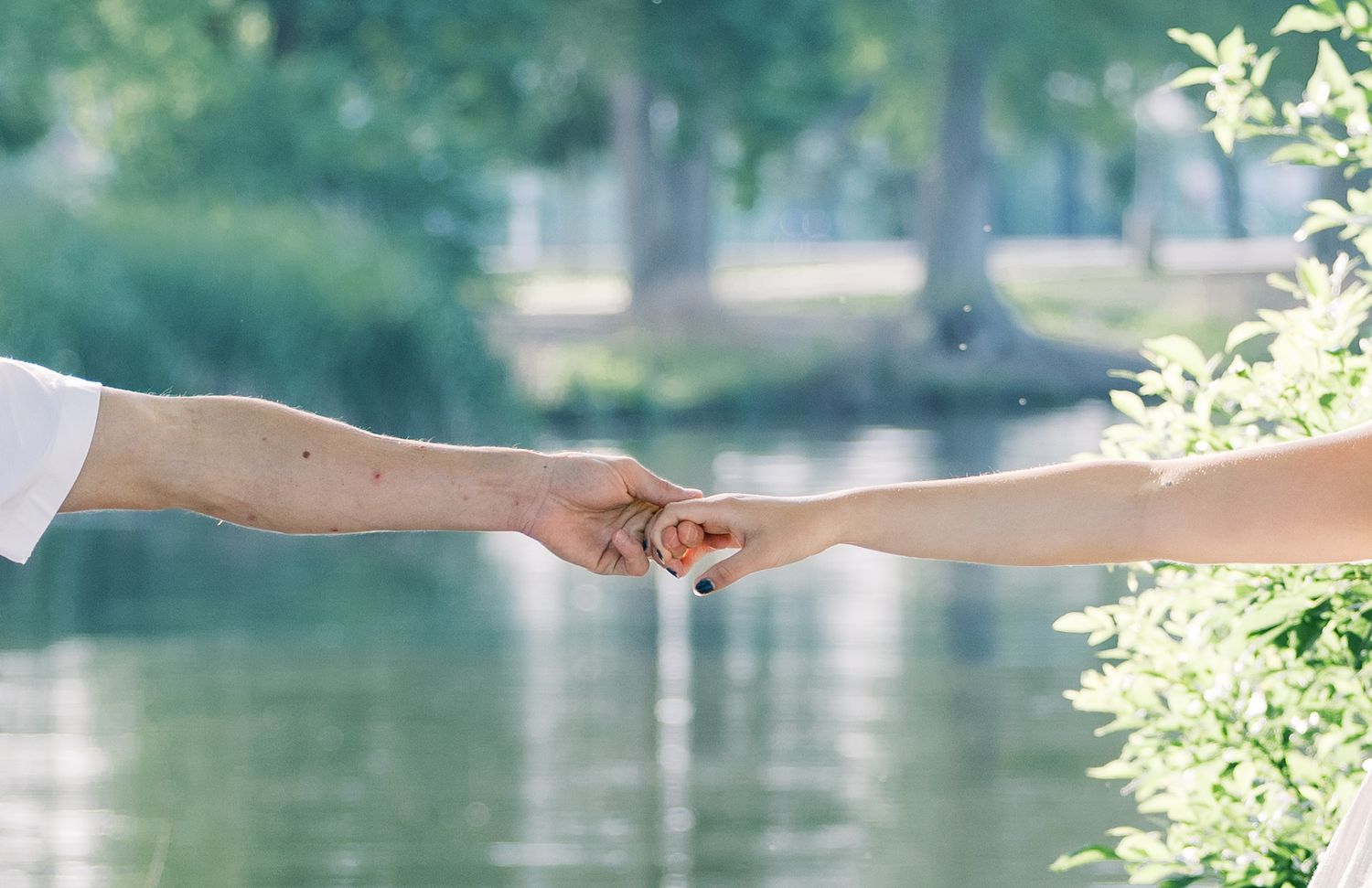 Two hands reaching out to hold each other with a serene lake in the background.