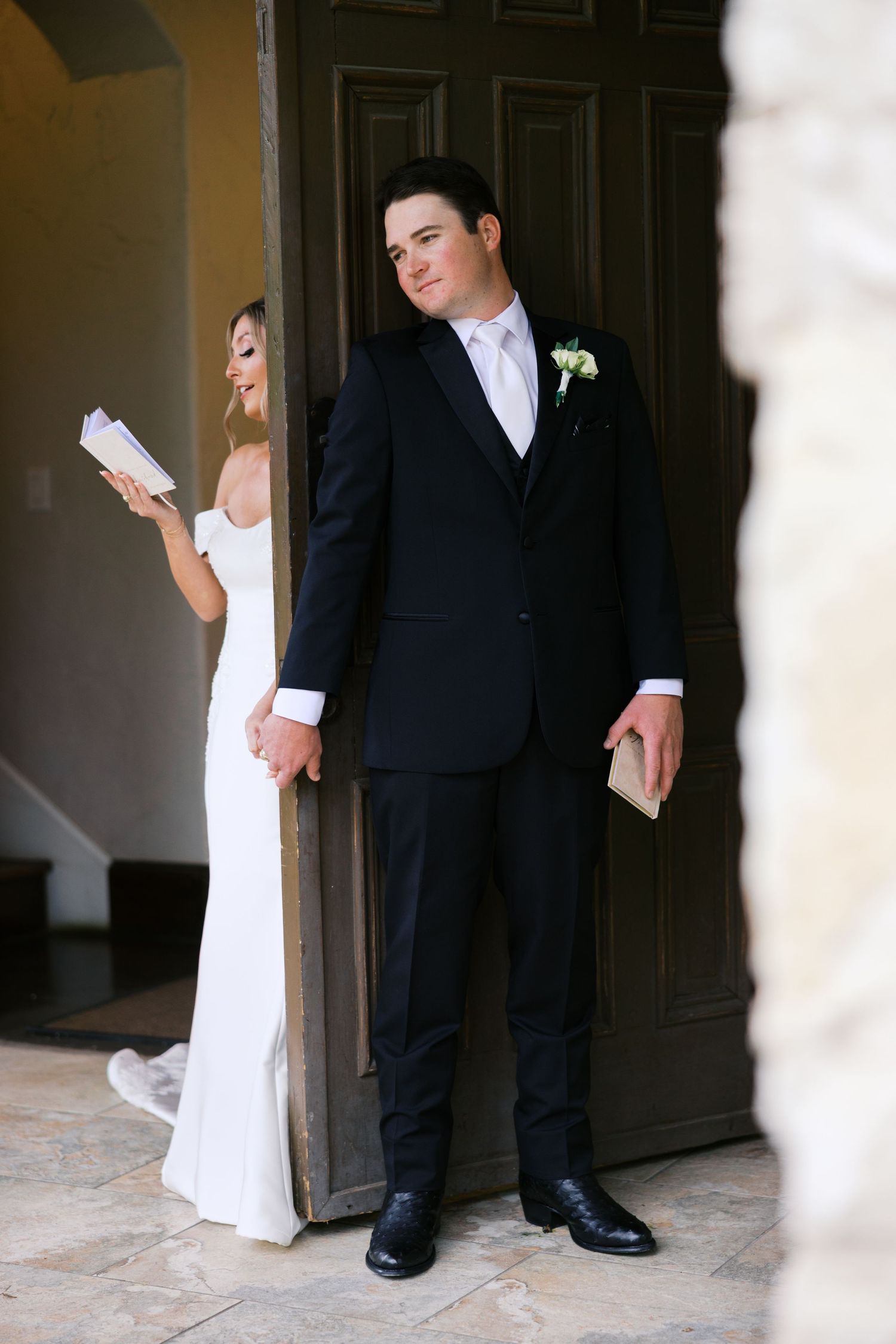 Bride and groom share private vows through a doorway, each holding letters, in a romantic first look moment.
