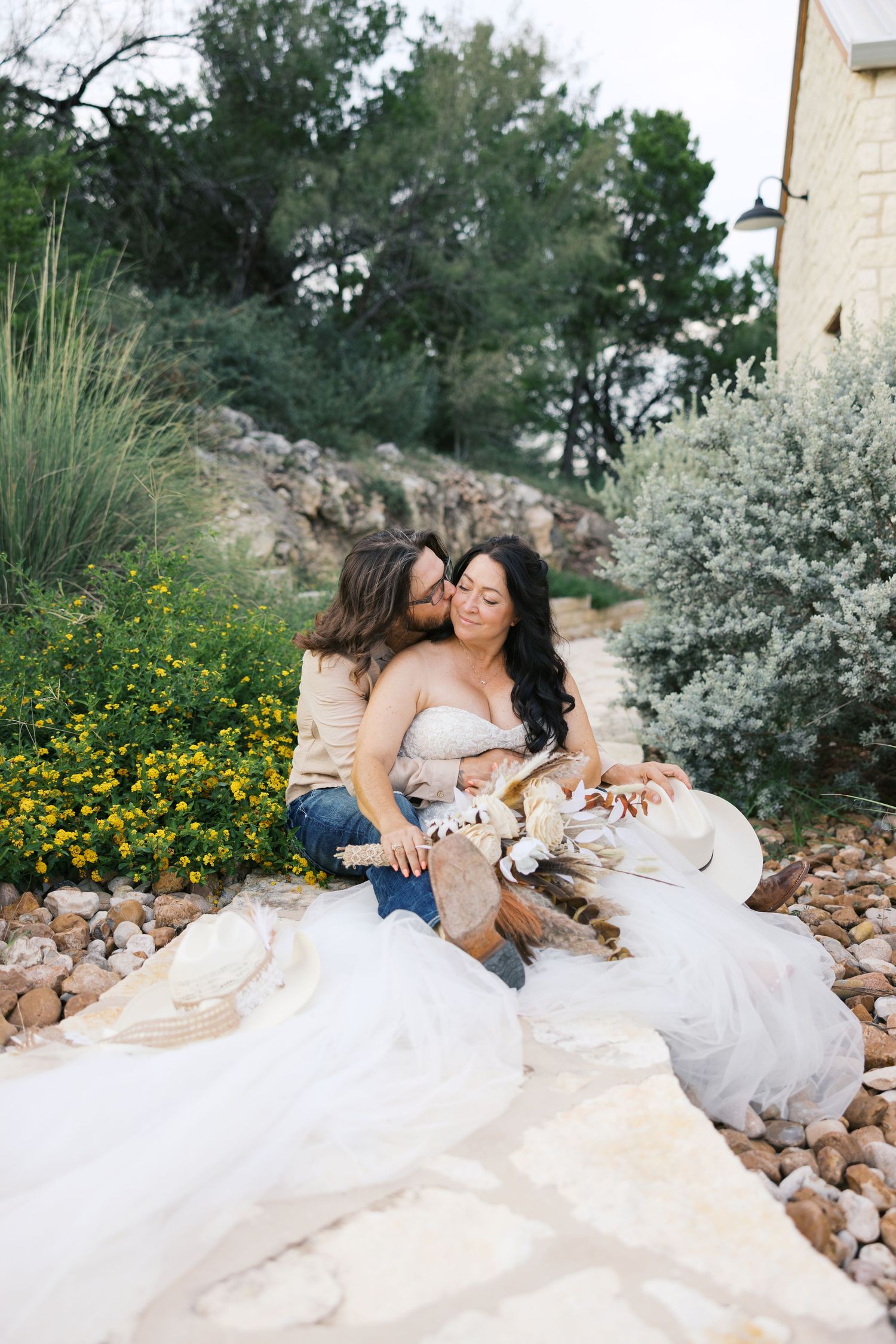 Wedding couple lounging on white rocks surrounded by yellow wildflowers and desert landscaping.