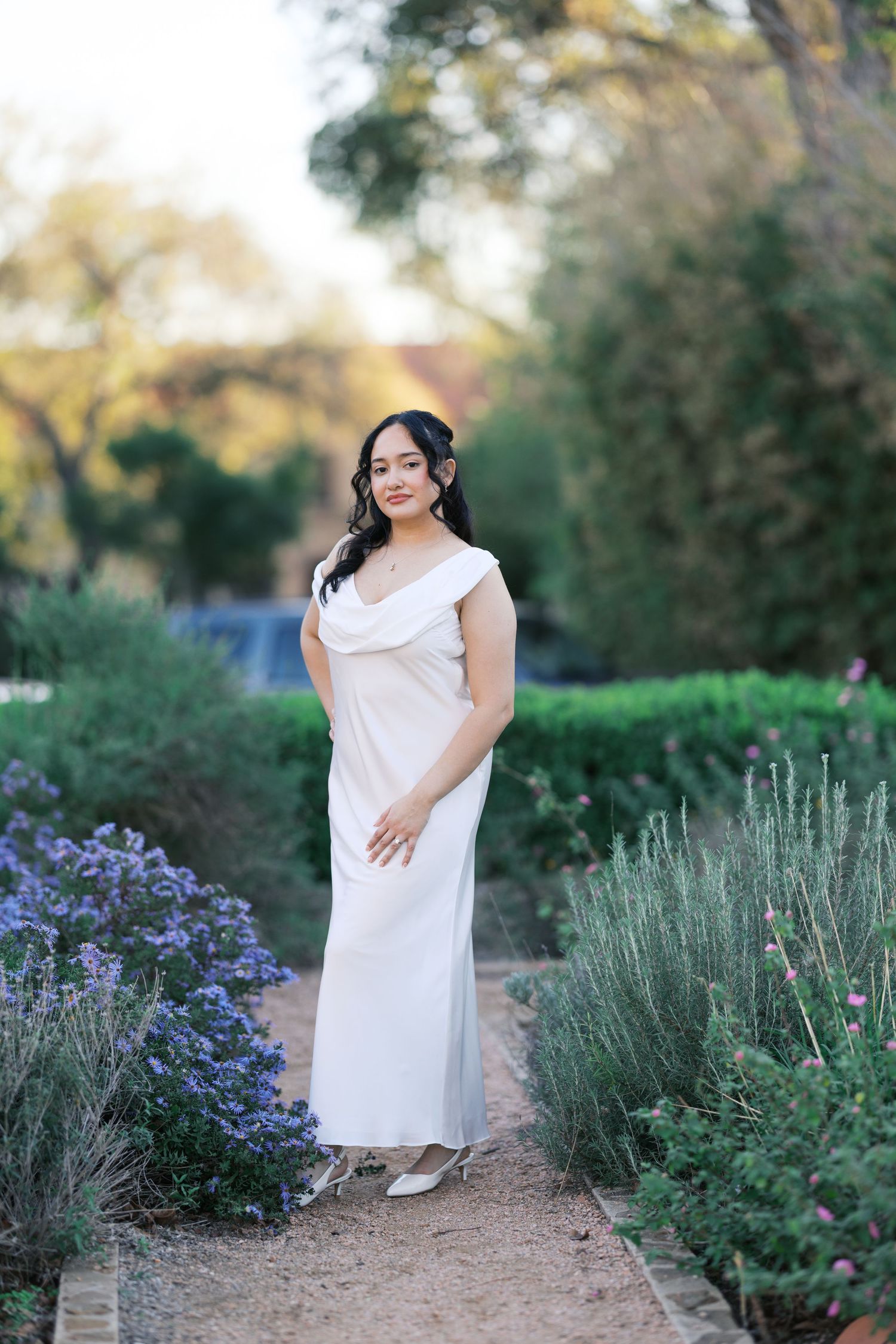 Bride poses elegantly among lavender and garden flowers in outdoor setting.
