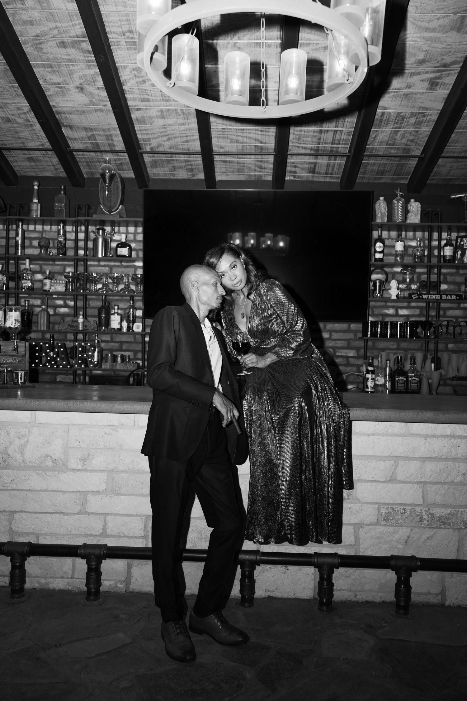 A couple shares a playful moment at a dimly lit bar with stone walls.