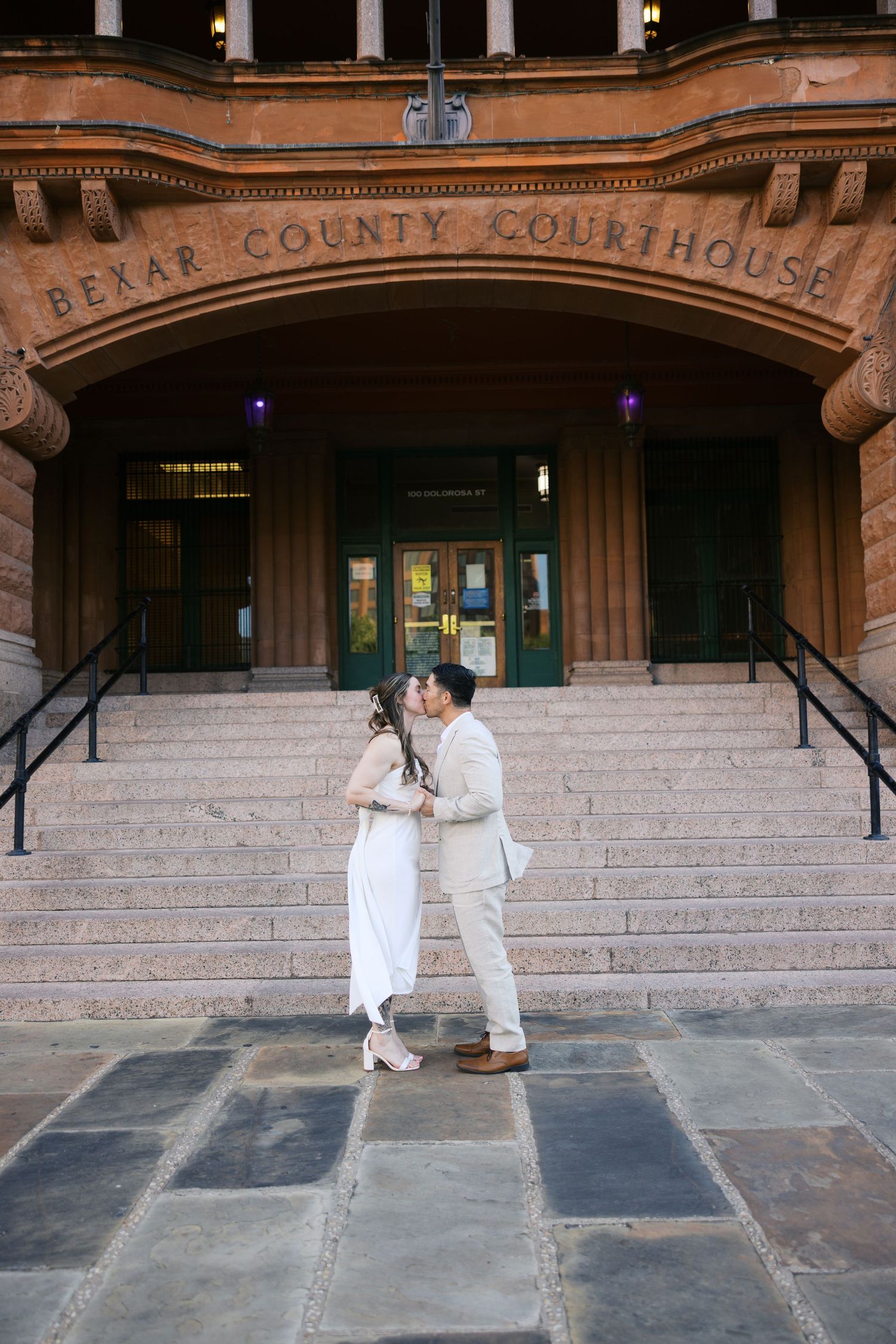 Couple in white outfits dancing in front of Bexar County Courthouse.