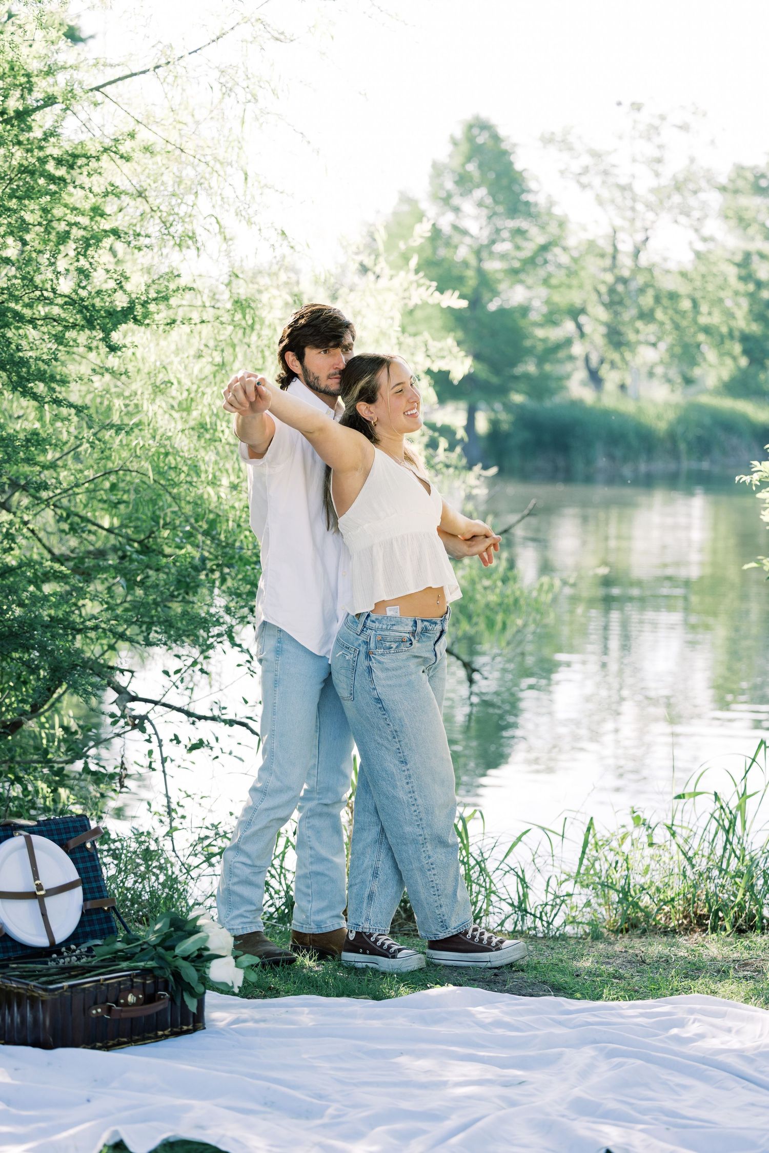A couple dances together on a white blanket near a peaceful lake.