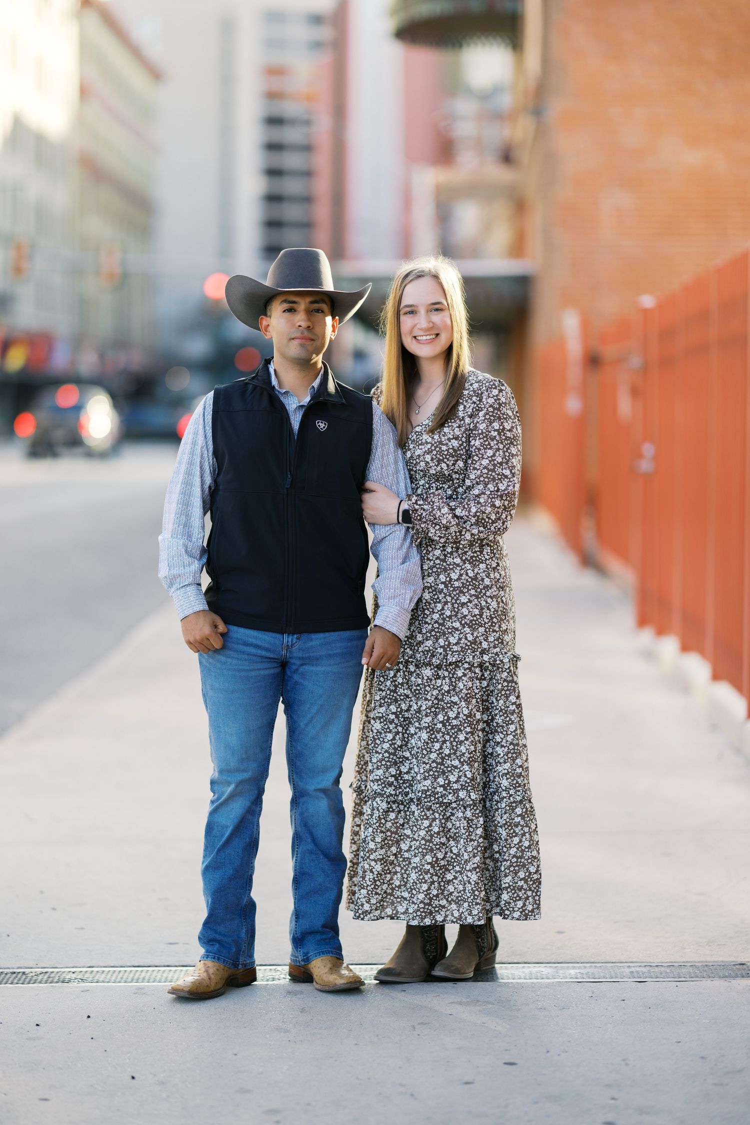 A couple walking together on a city sidewalk with brick buildings in the background.