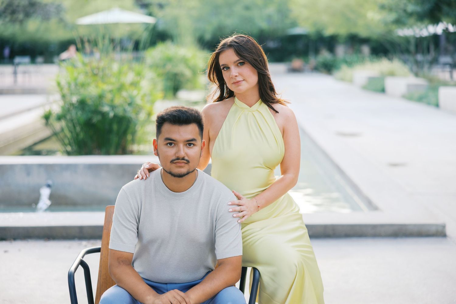 A couple poses outdoors in casual attire near a white building.