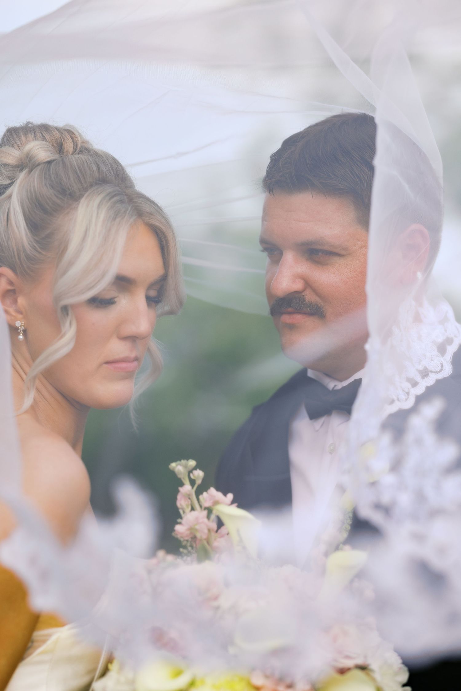 Bride and groom share an intimate moment together under a flowing white wedding veil.