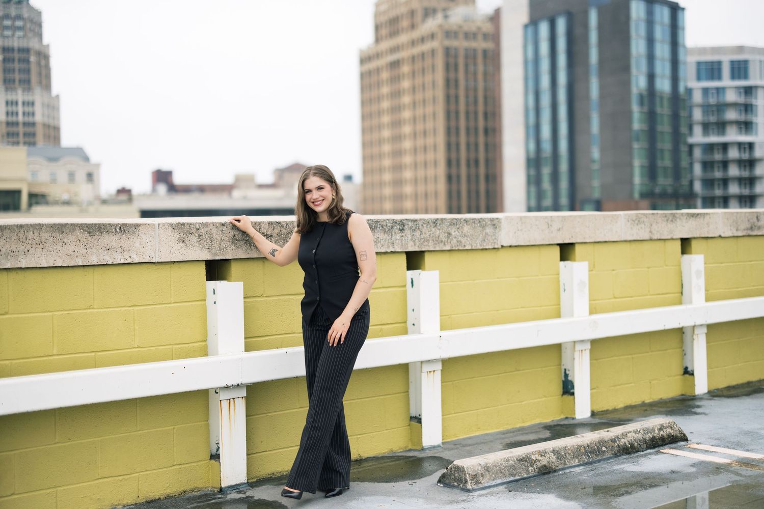 Professional fashion photoshoot on a rooftop parking deck with city buildings in the background.