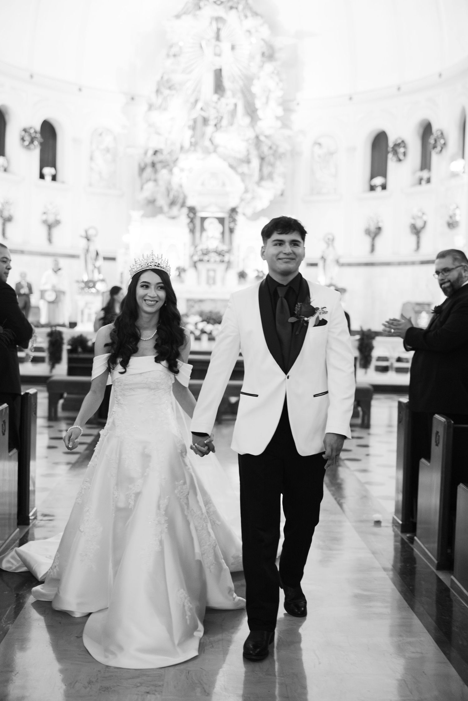 Newlyweds walking down church aisle after ceremony with ornate altar in background.