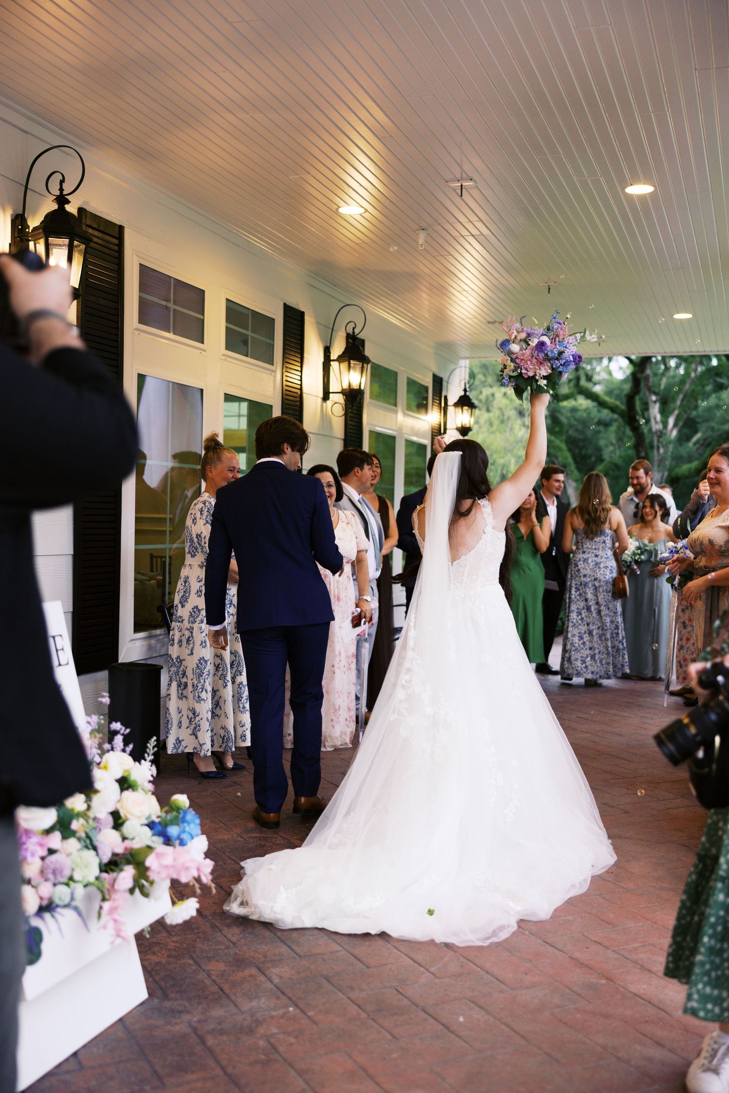 Wedding reception guests dancing and celebrating on an outdoor covered patio with floral decorations.