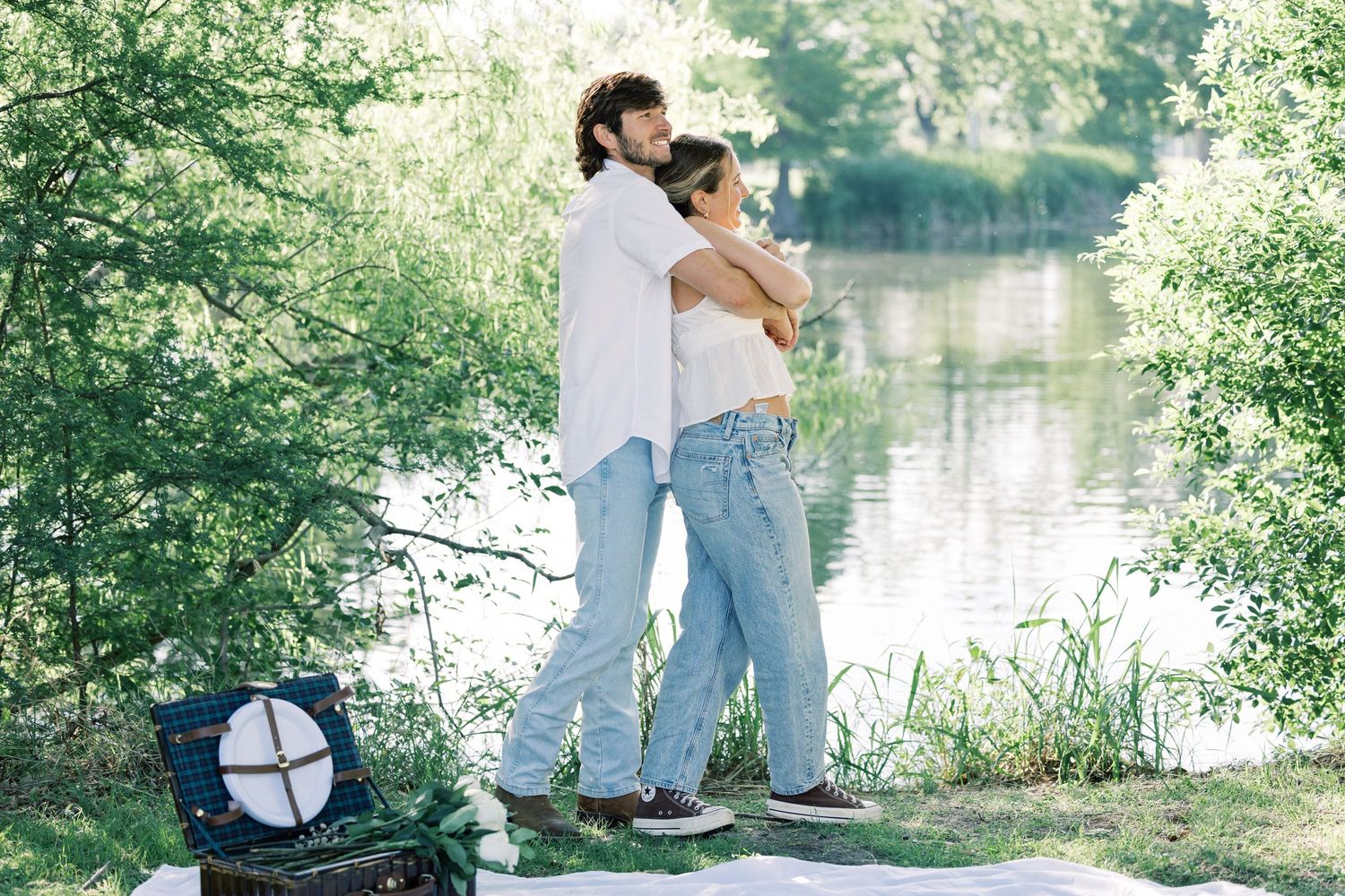 A couple enjoys a sunny afternoon by the water's edge in casual denim and white attire.