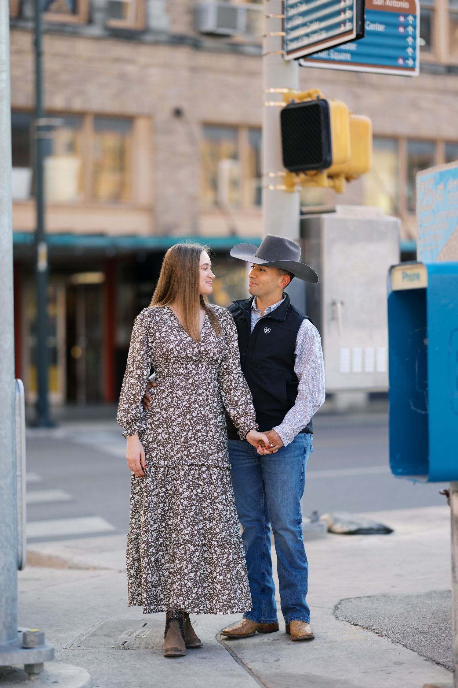 A couple walking hand in hand on an urban sidewalk with traffic signals in view.
