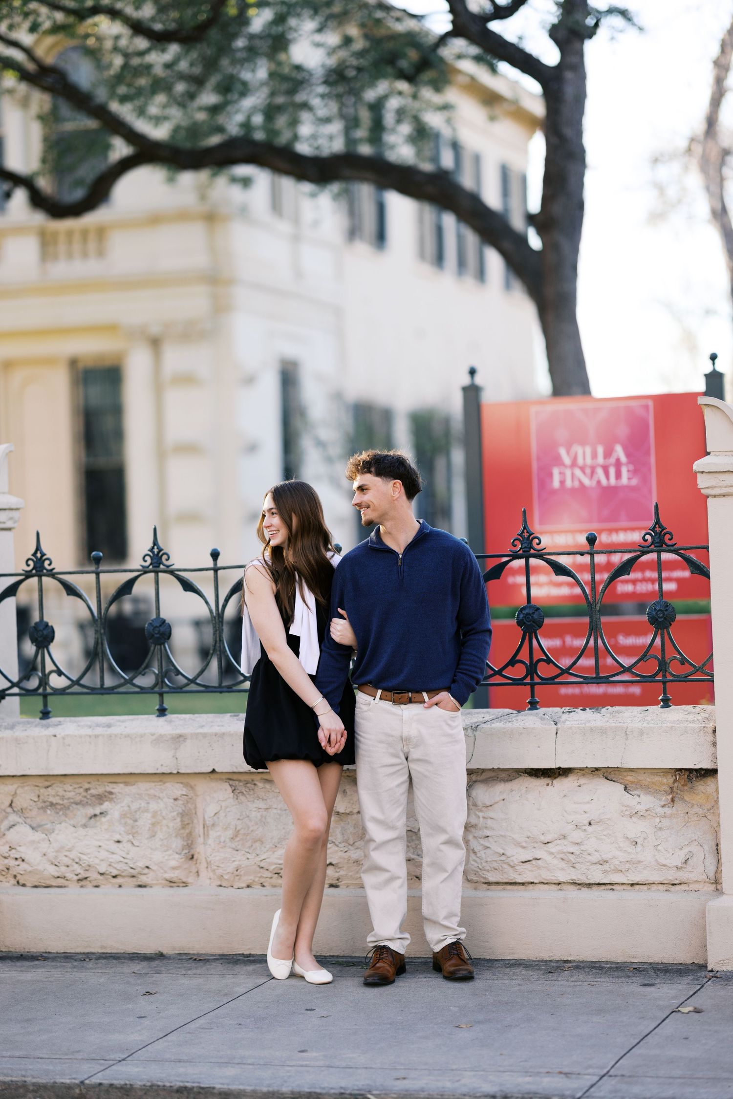 Young couple standing together on a sidewalk near an ornate iron fence outside Villa Finale.