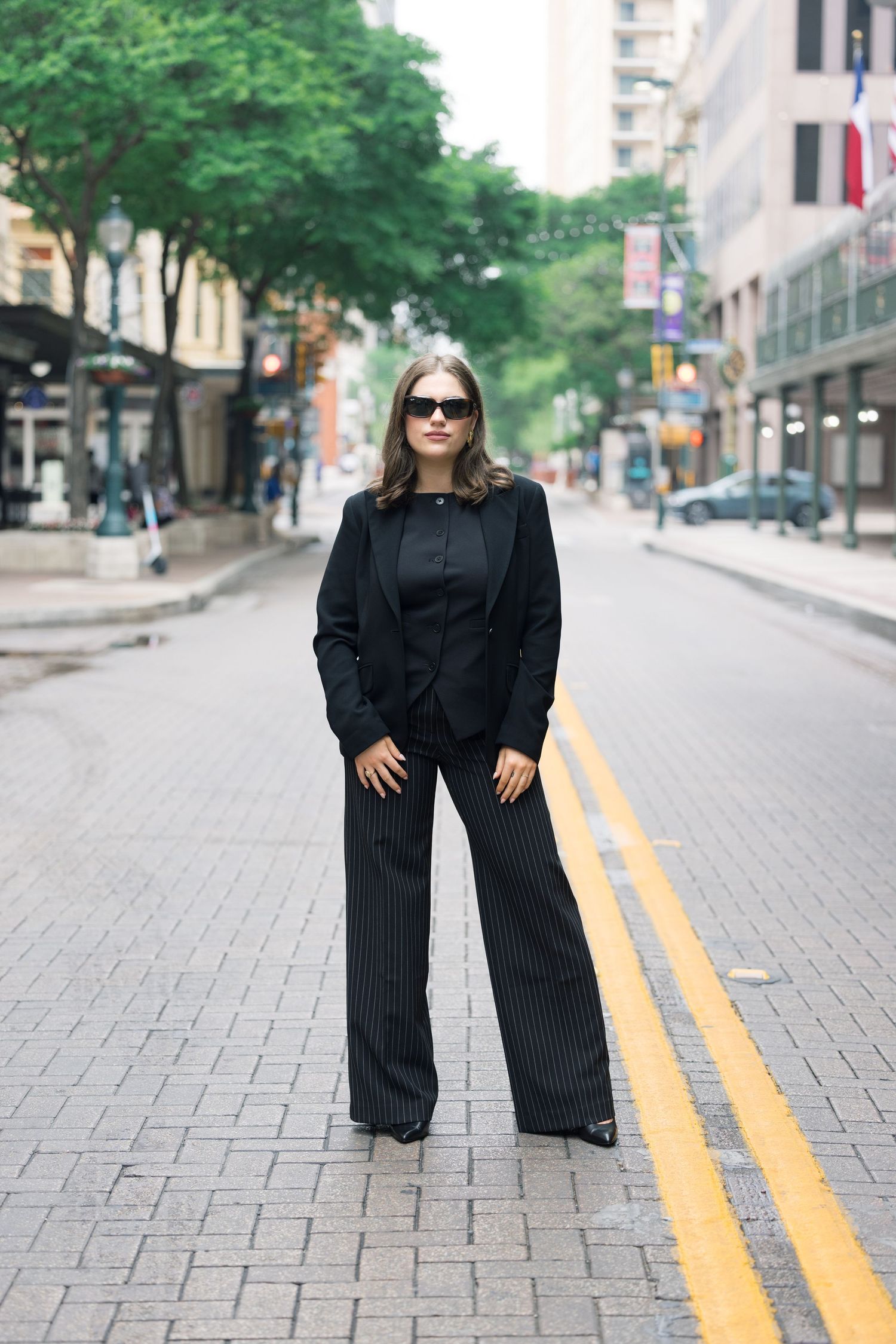 Stylish black pantsuit outfit worn on an urban street with yellow lines and trees.