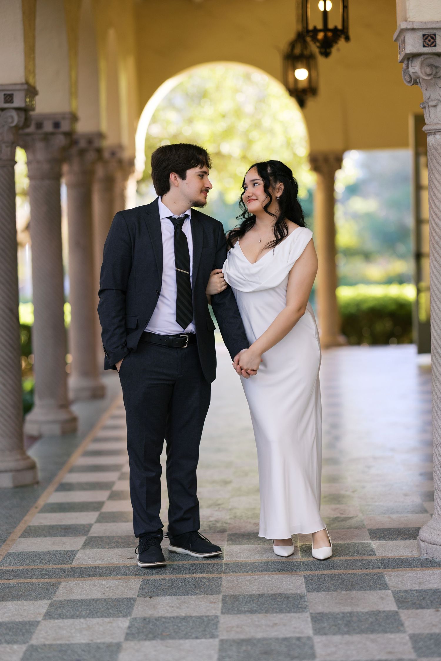 A couple shares romantic moments in an elegant colonnade with checkerboard floor.