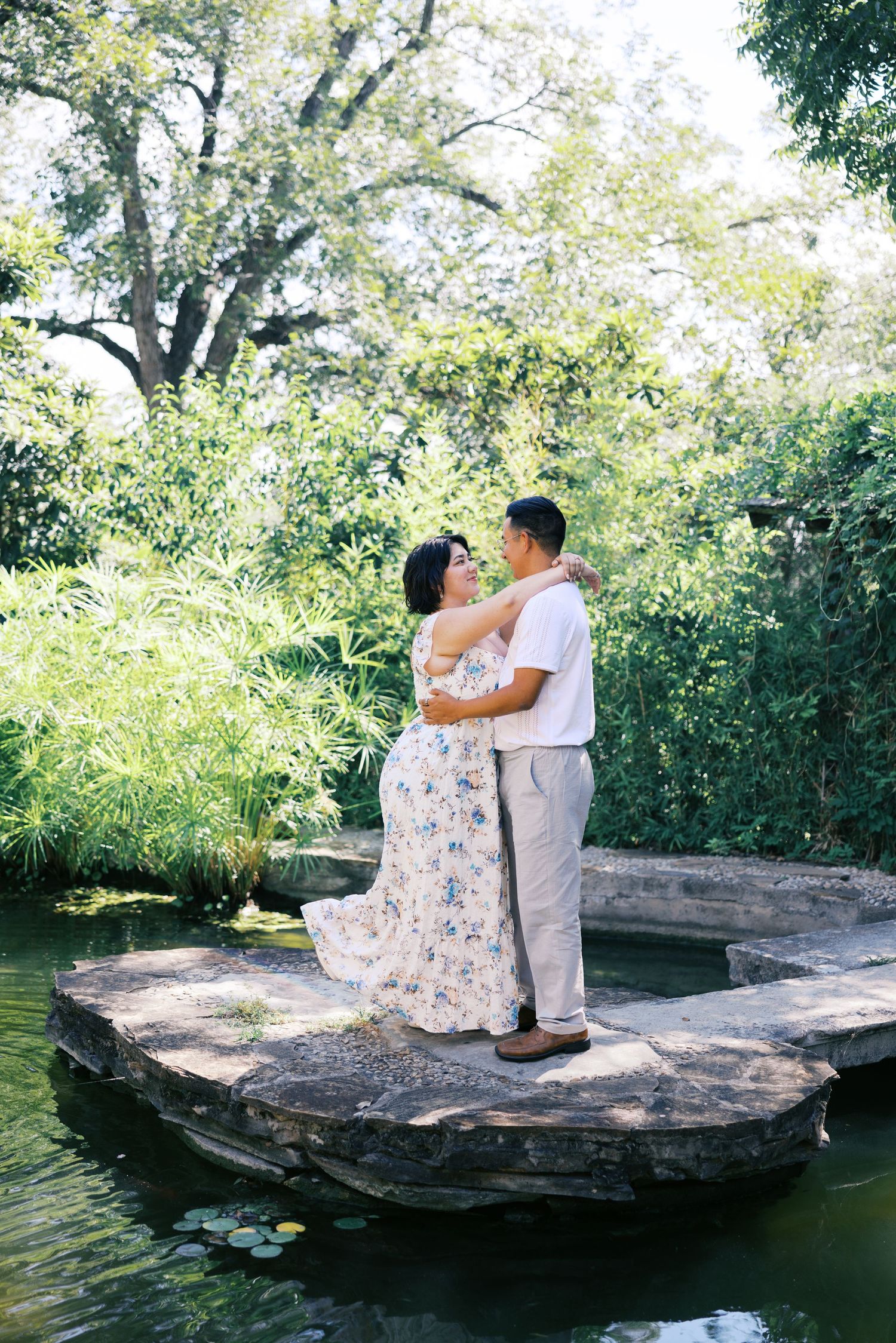 A romantic garden photoshoot on a stone platform with water reflections and green foliage.