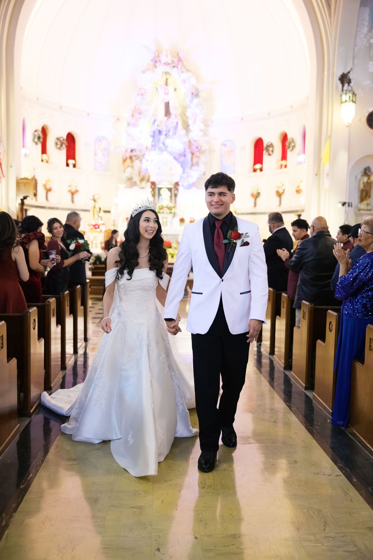 A couple walking down the church aisle after their wedding ceremony with guests seated in pews.