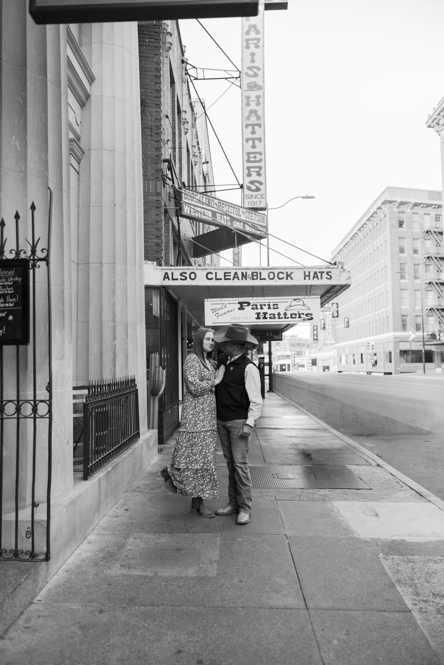 A couple poses in front of a vintage storefront with retro signage.