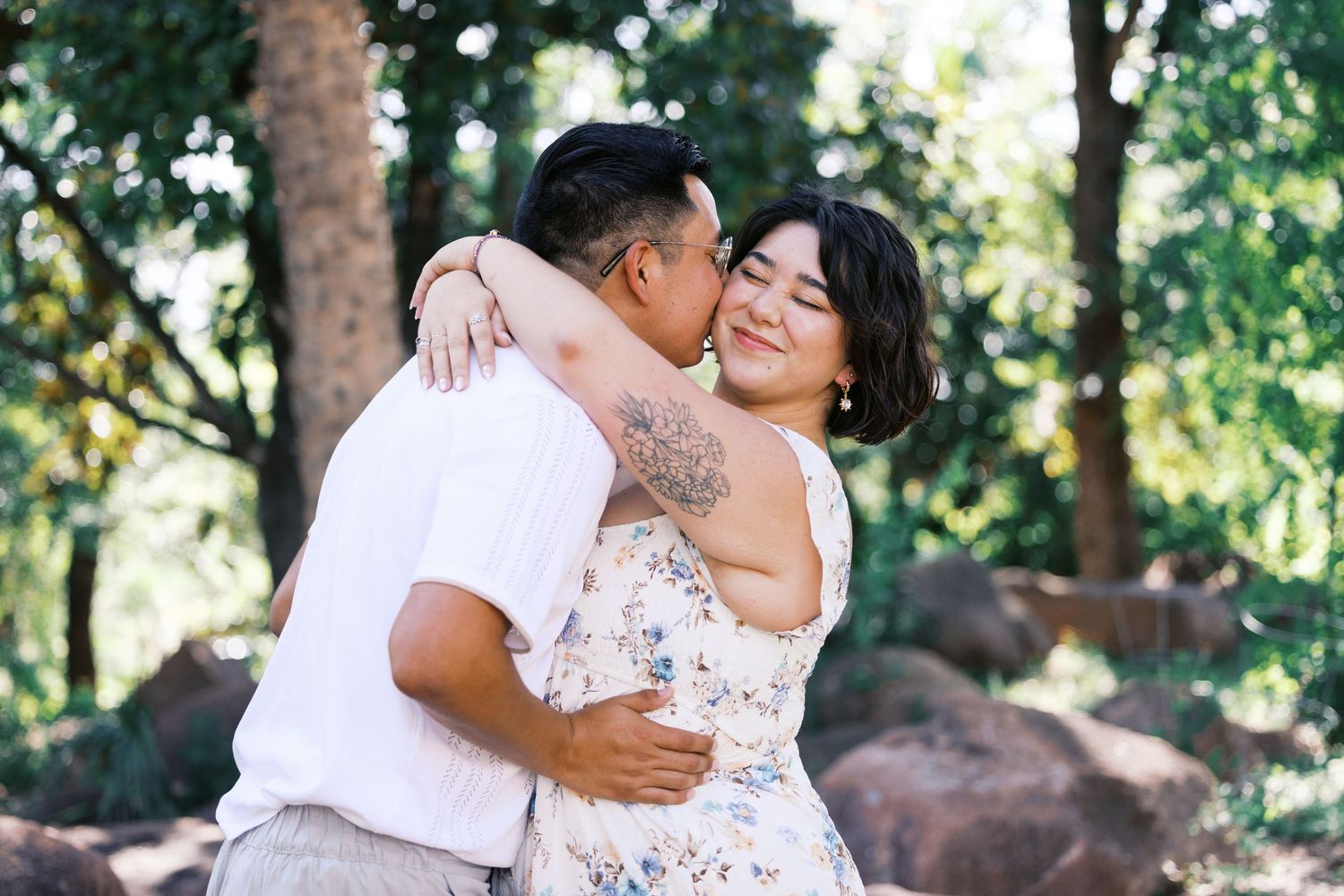 A romantic embrace between a couple in a garden setting with trees in the background.