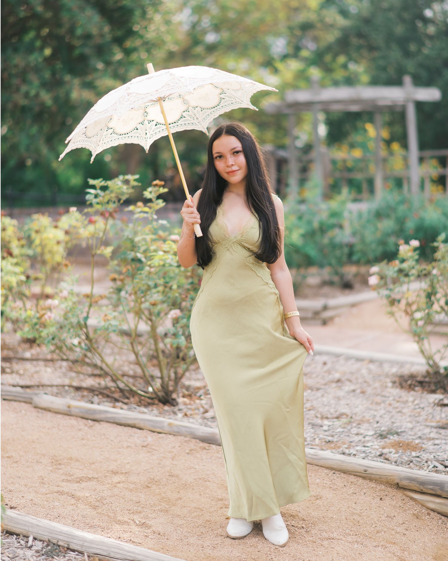 Woman in pale yellow dress holding lace parasol in garden setting.