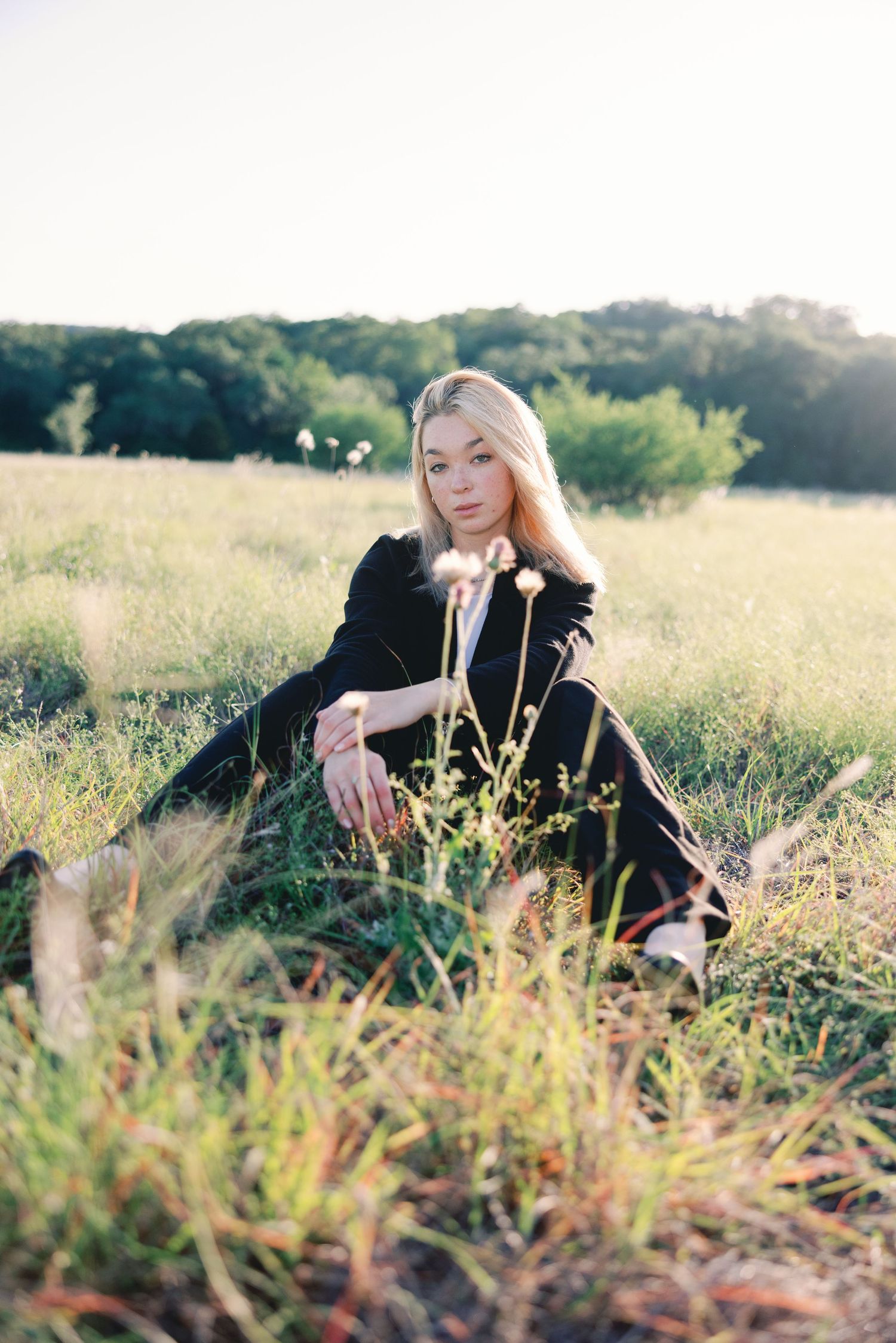 Person in black outfit reclining in tall grass during sunset in meadow.