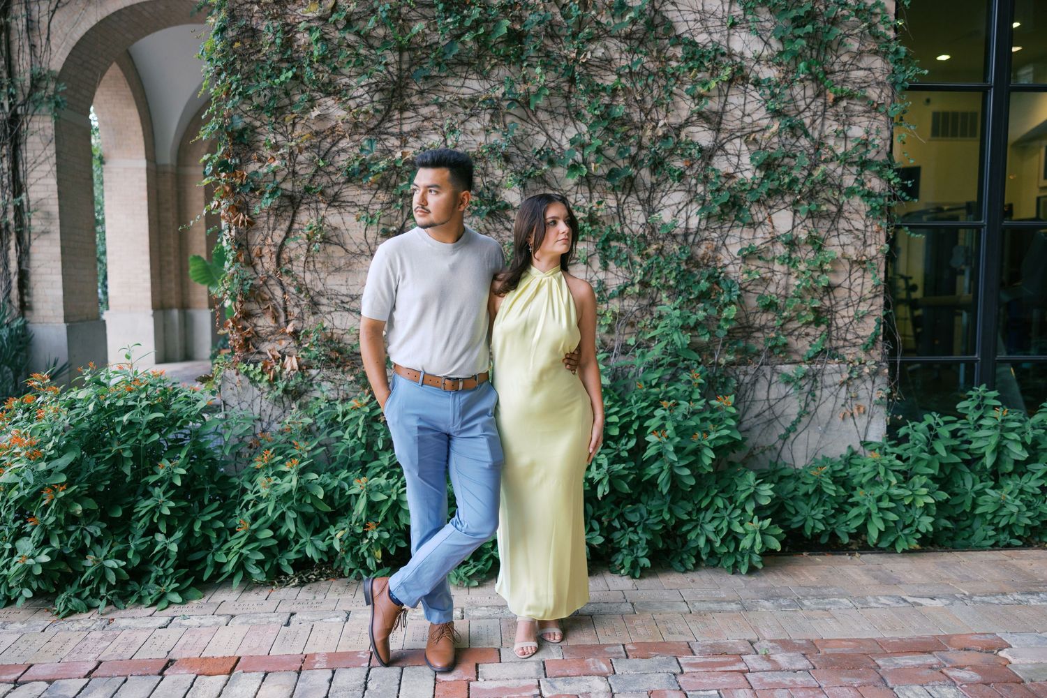 Couple posing against ivy-covered wall during outdoor photoshoot.