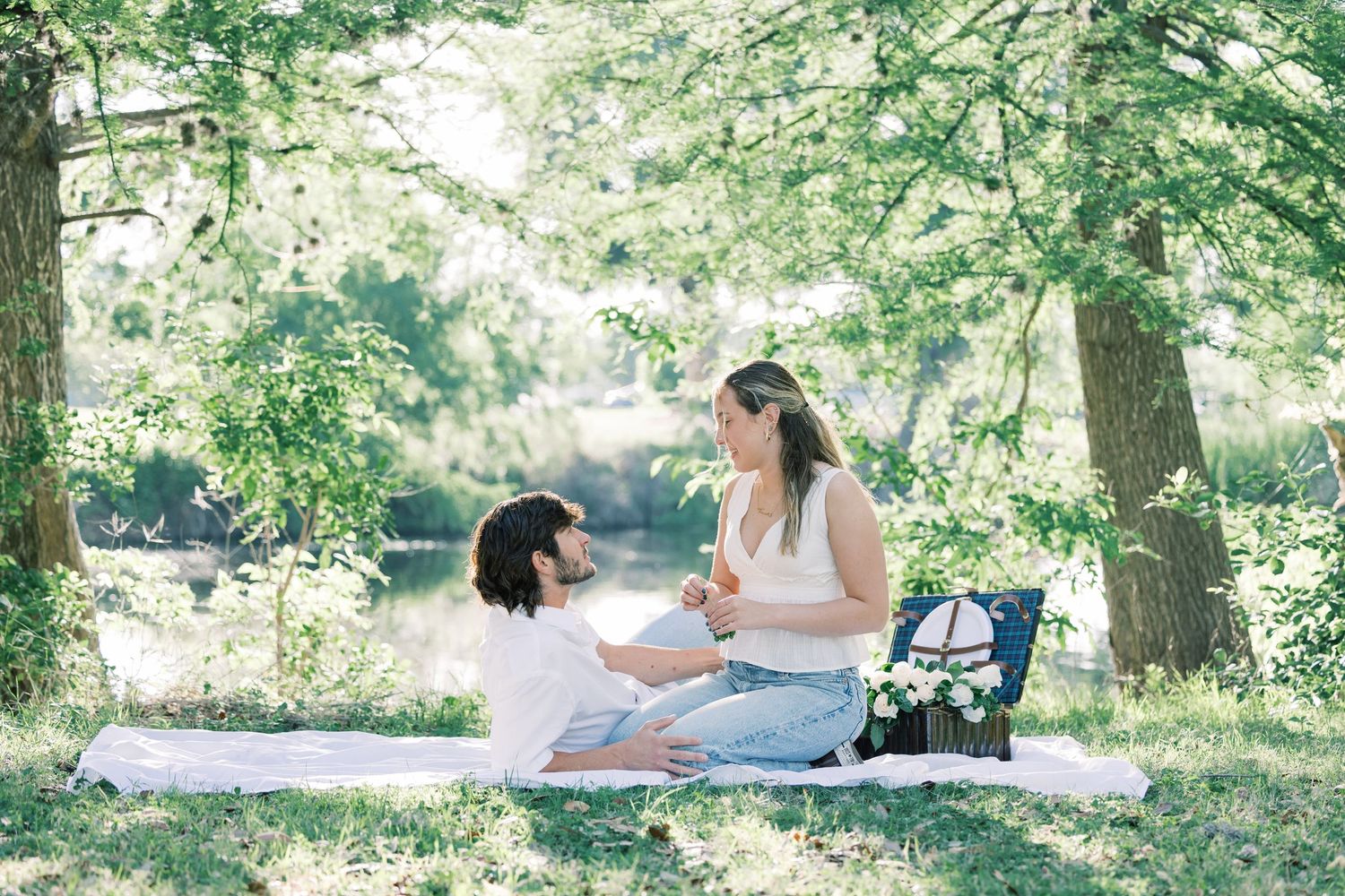 A couple relaxes on a picnic blanket surrounded by green trees and natural scenery.