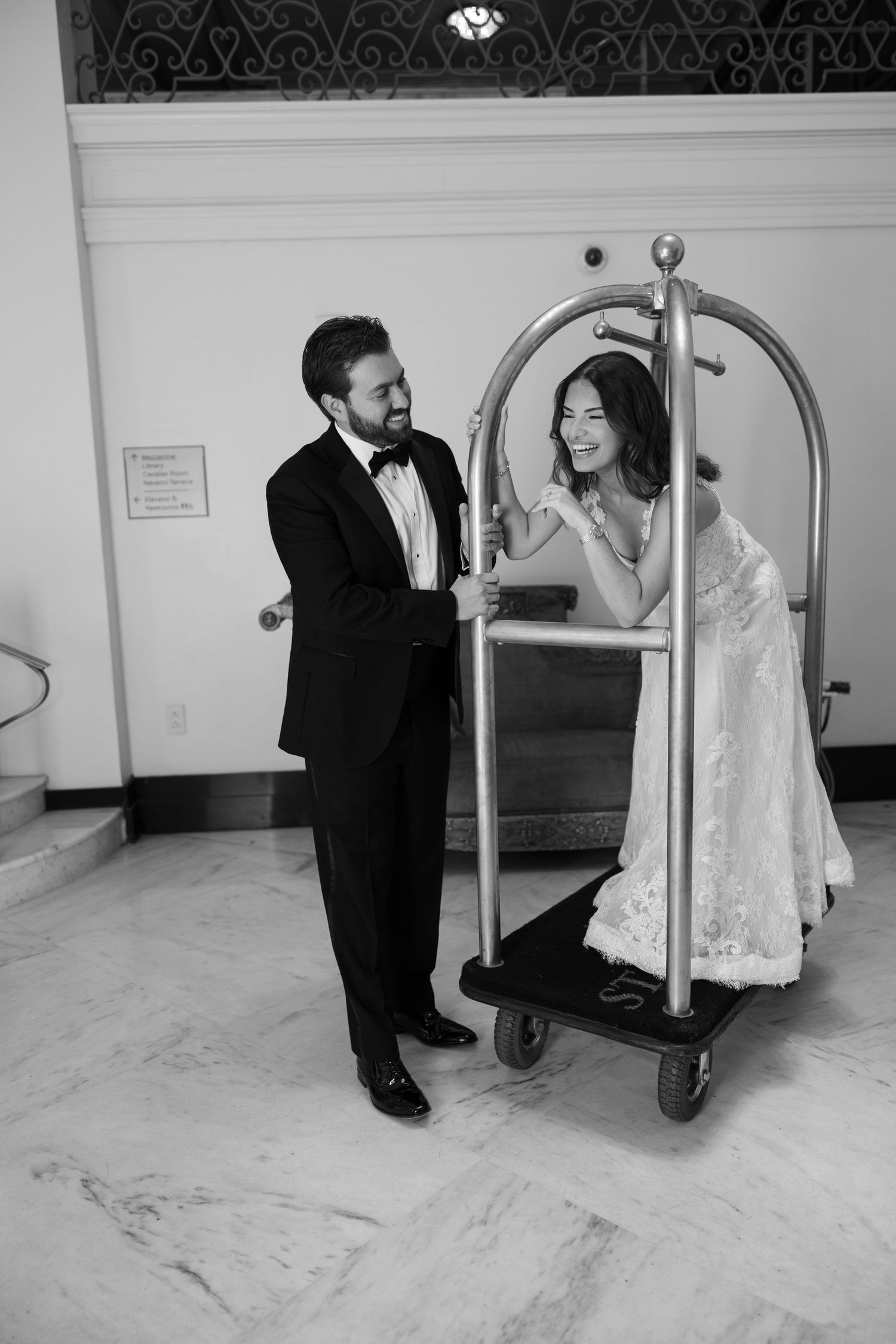 Black and white sequence of playful moments between a couple with a luggage cart in a hotel hallway.