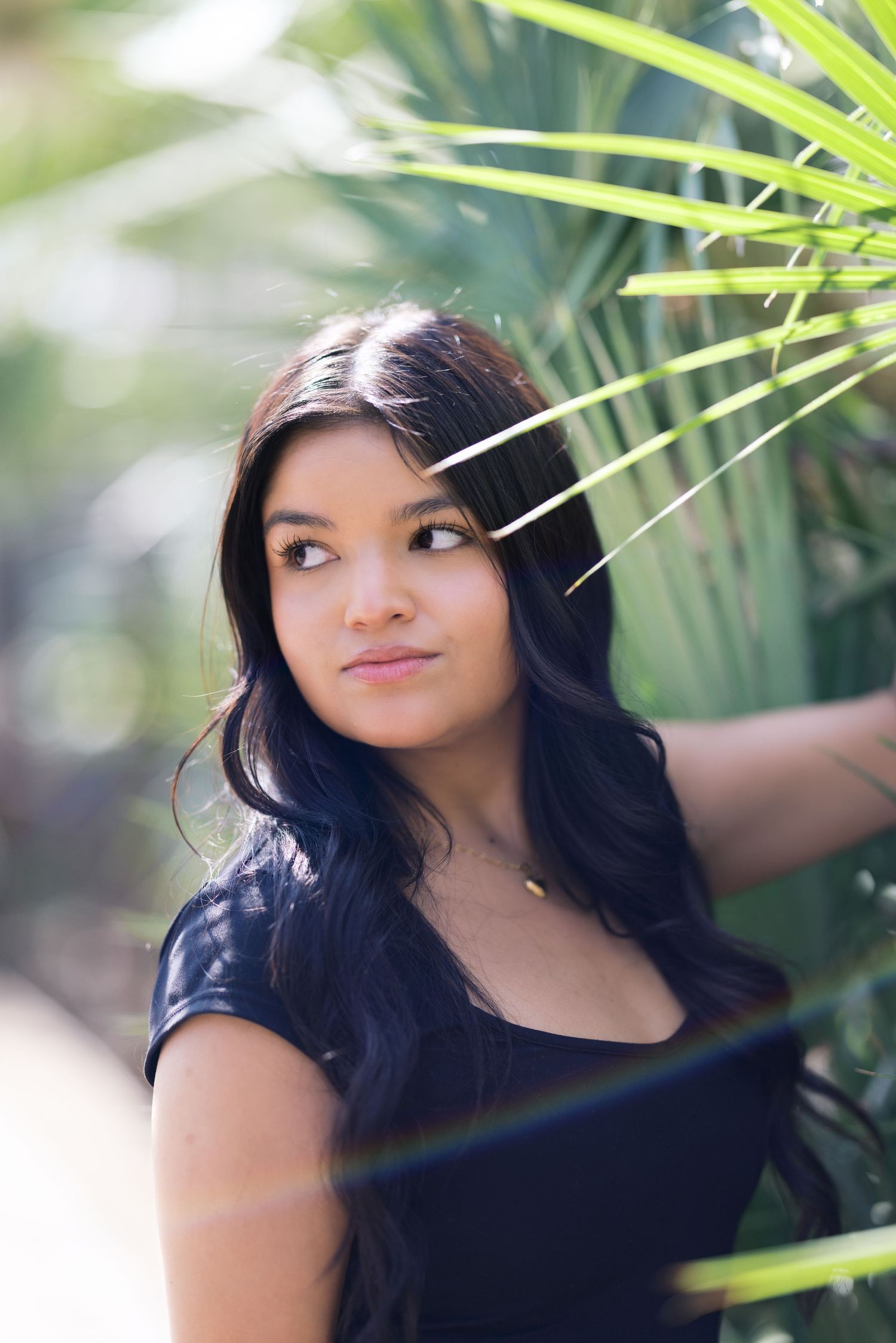 Close-up portrait with palm fronds creating natural frame in outdoor setting.
