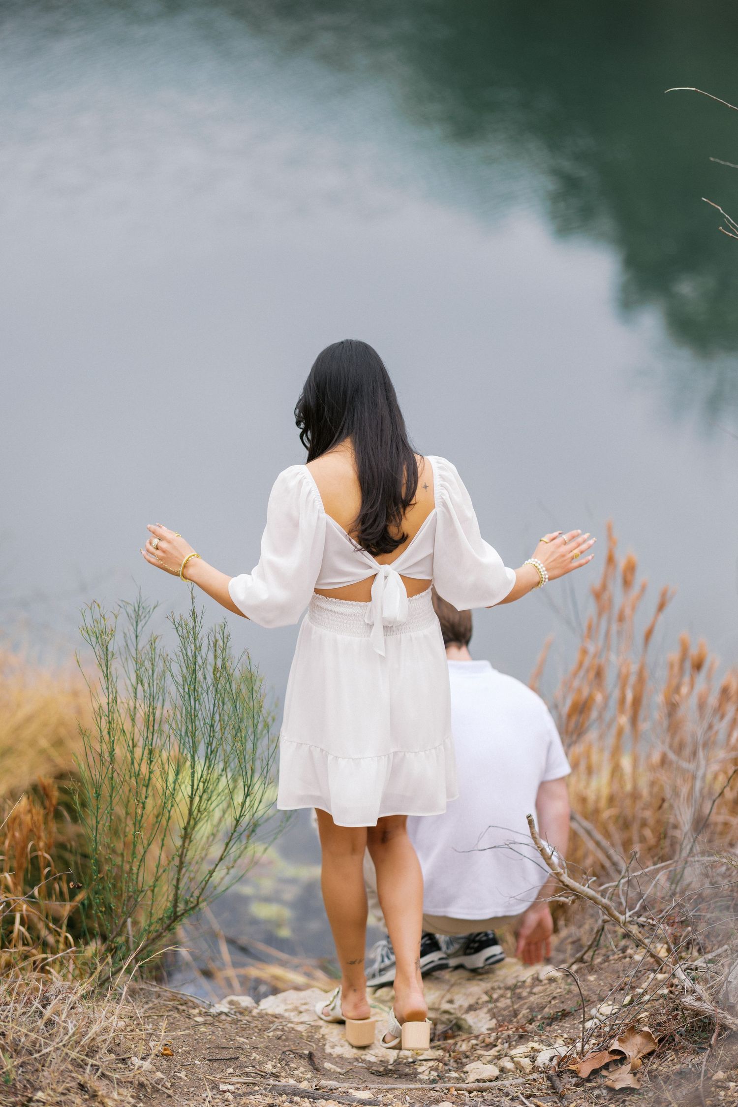 Couple in white outfits exploring rocky terrain by peaceful lake waters.