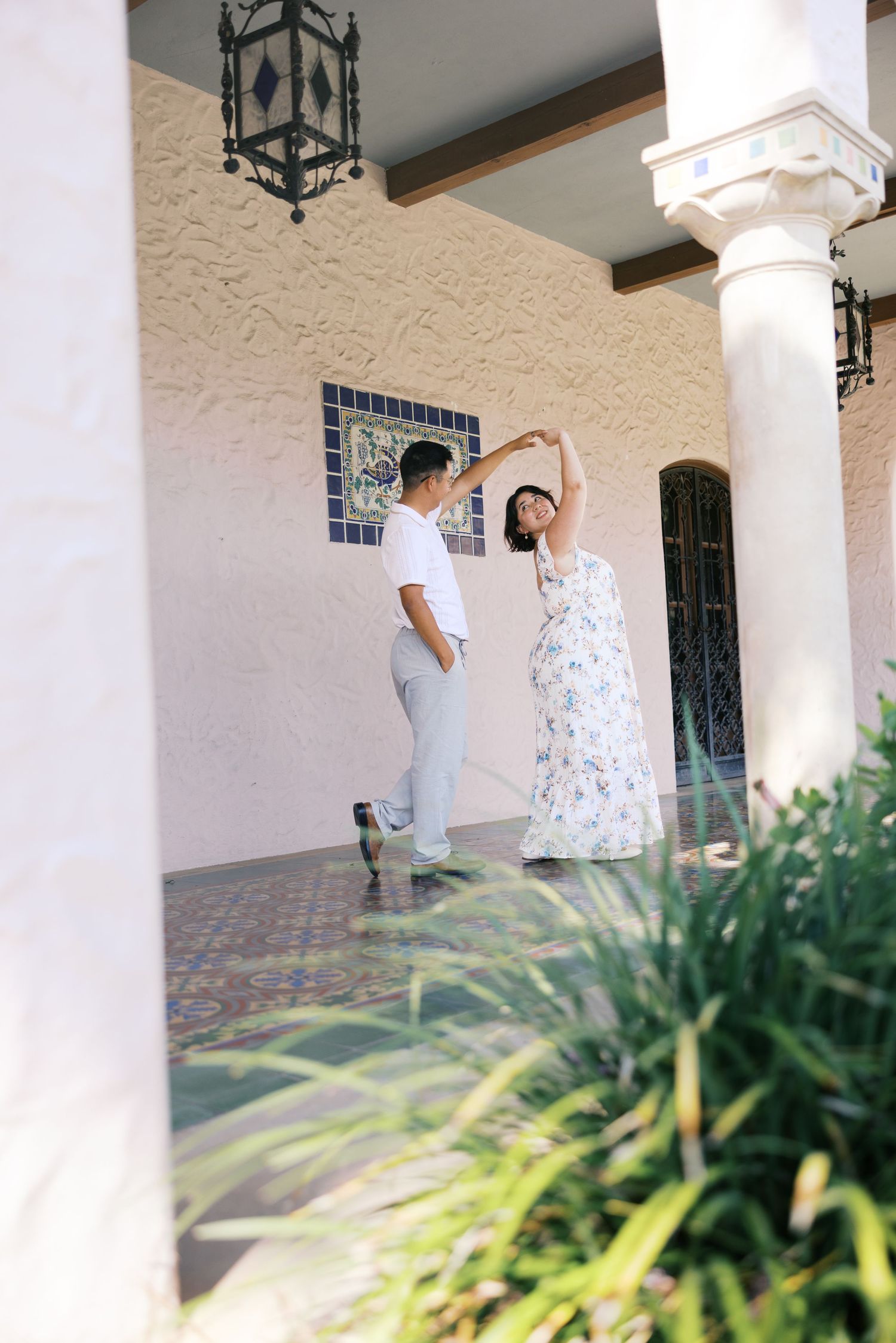 A couple dances on a covered patio with Spanish colonial architecture and decorative lanterns.