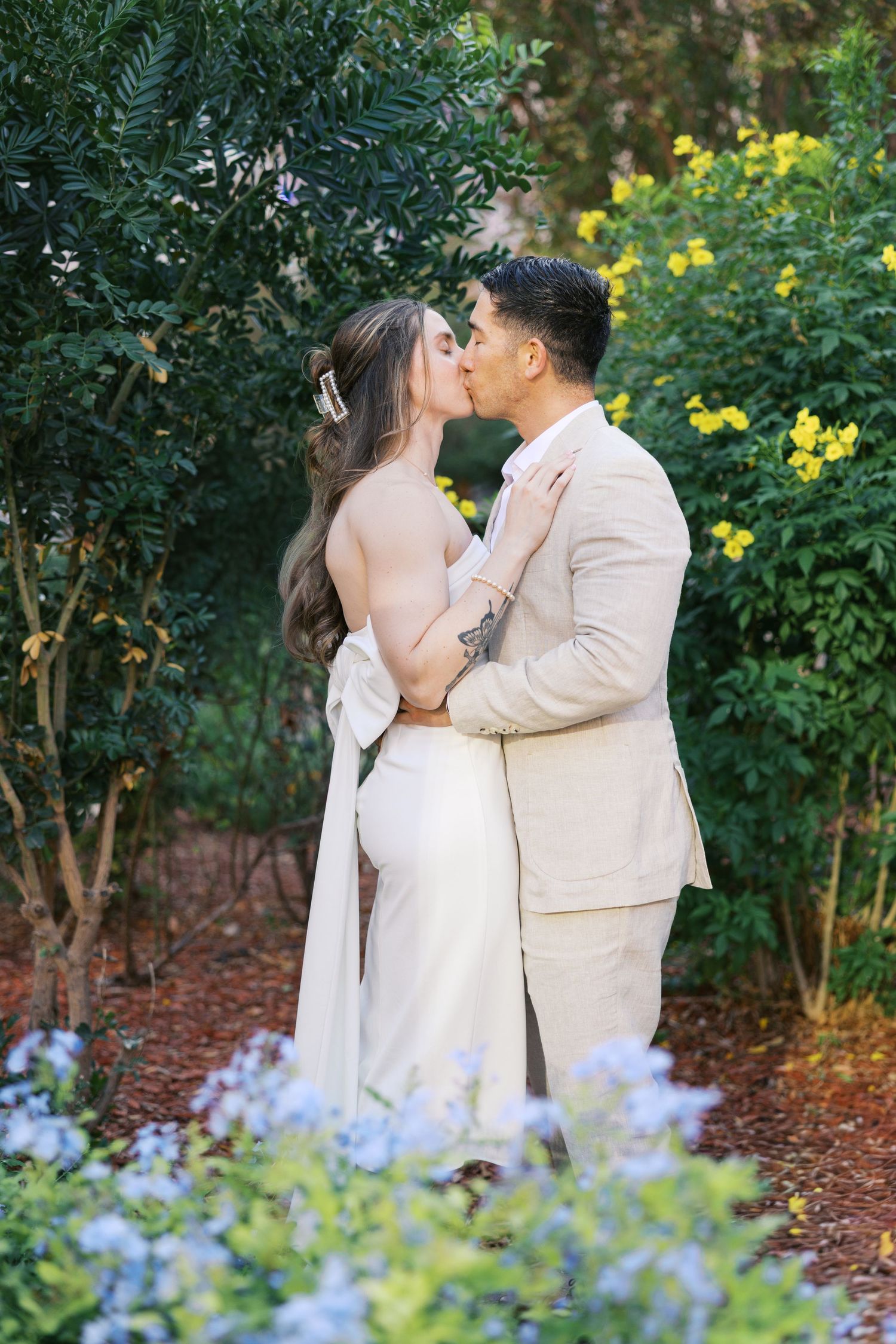 A romantic garden wedding photo with a couple embracing among yellow flowers and greenery.