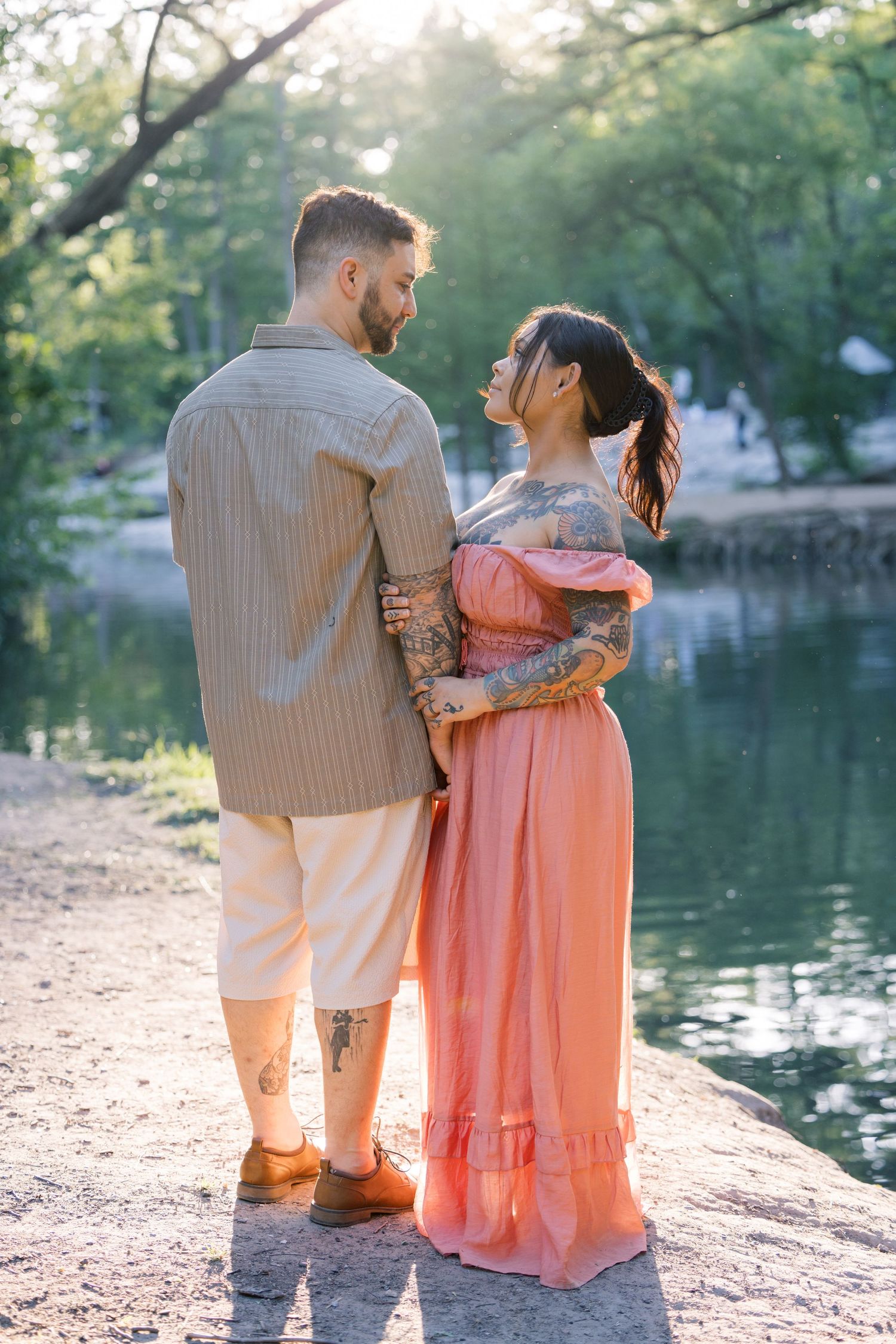 Two people in complementary outfits share a tender moment beside a peaceful lake.