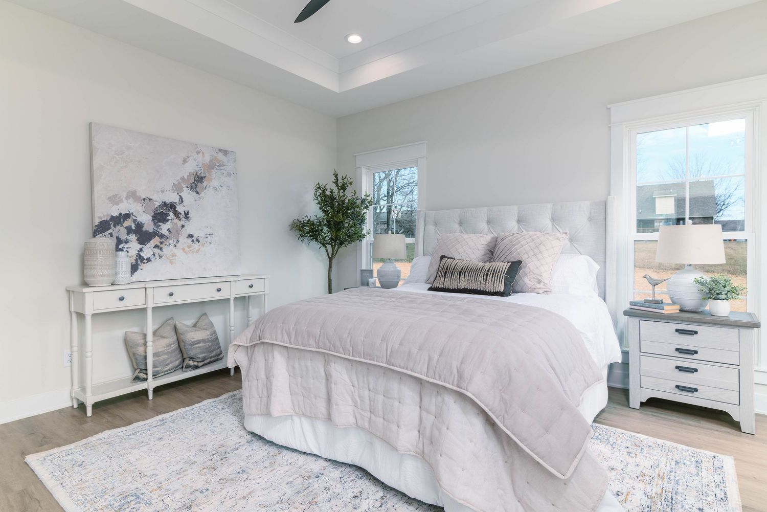 Serene master bedroom with tray ceiling, upholstered headboard, gray decor, and hardwood floors.