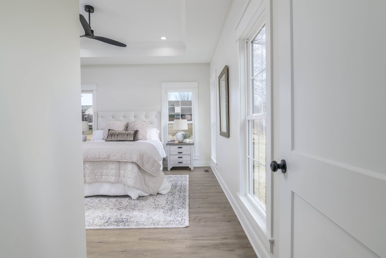 Bright master bedroom entrance with hardwood floors, white walls, and natural light from large windows.