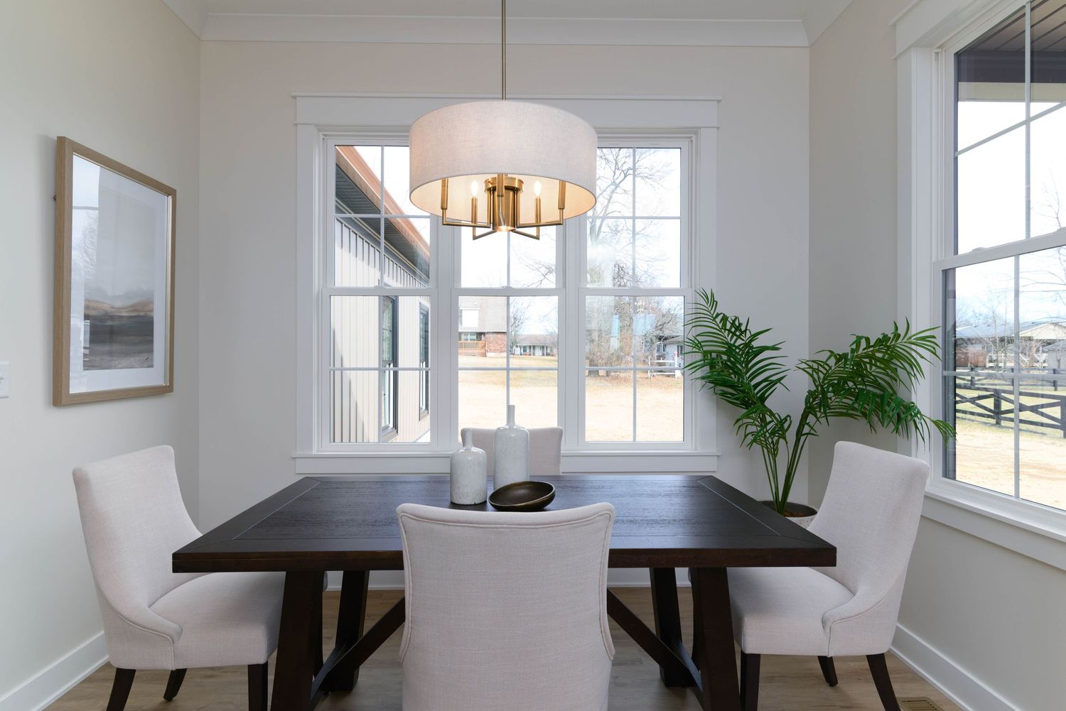 Elegant dining room with dark wood table, white upholstered chairs, and large windows with natural light.