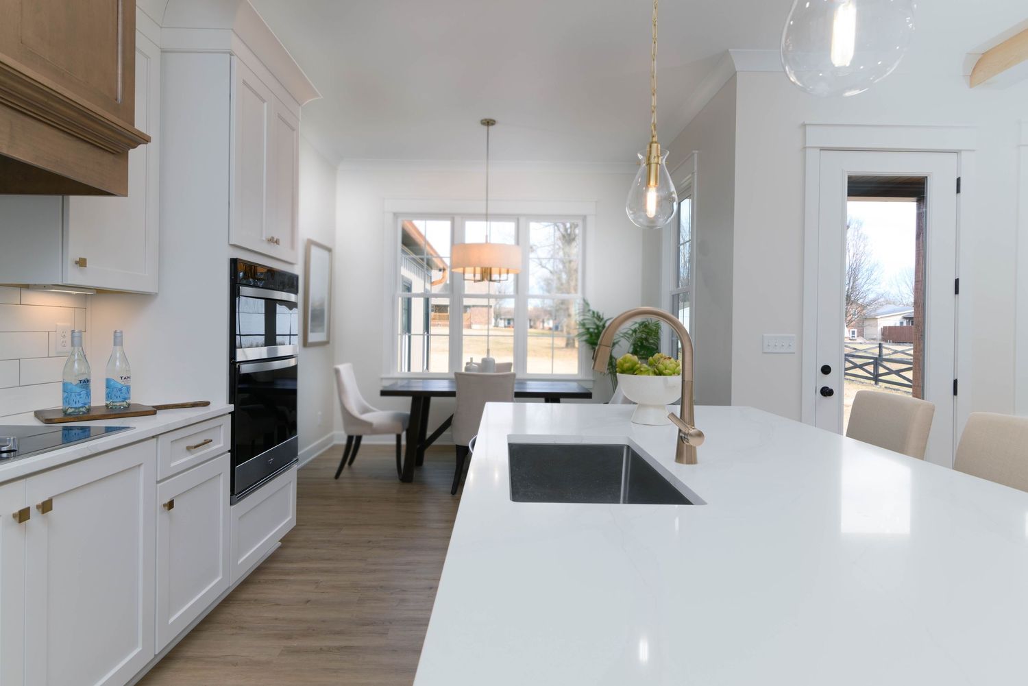 Contemporary kitchen with white quartz island, gold faucet, pendant lighting, and view of dining area beyond.