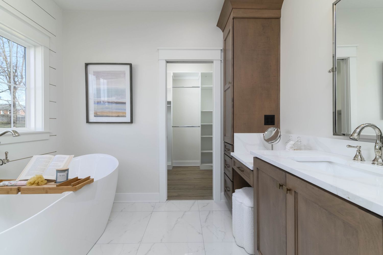 Elegant master bathroom with freestanding soaking tub, marble tile floors, wood vanity, and walk-in closet.