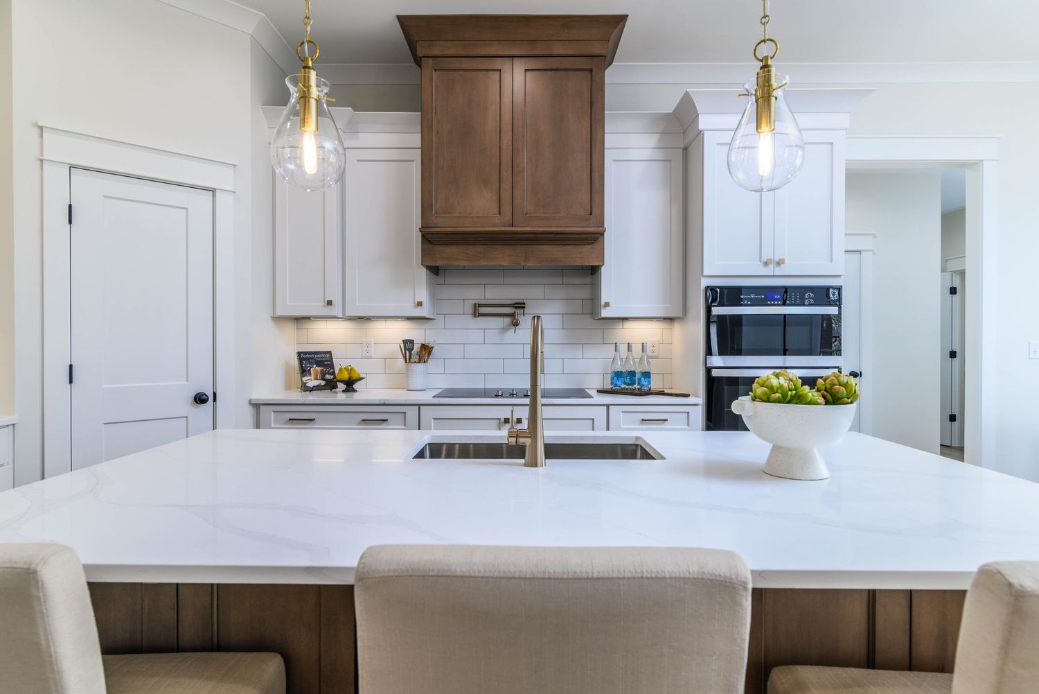 Modern kitchen island with white quartz countertop, gold pendant lights, and warm wood cabinetry accents.
