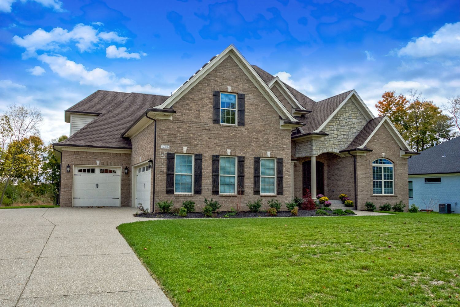 Elegant two-story brick home with manicured lawn, attached garage, and mature trees in autumn.