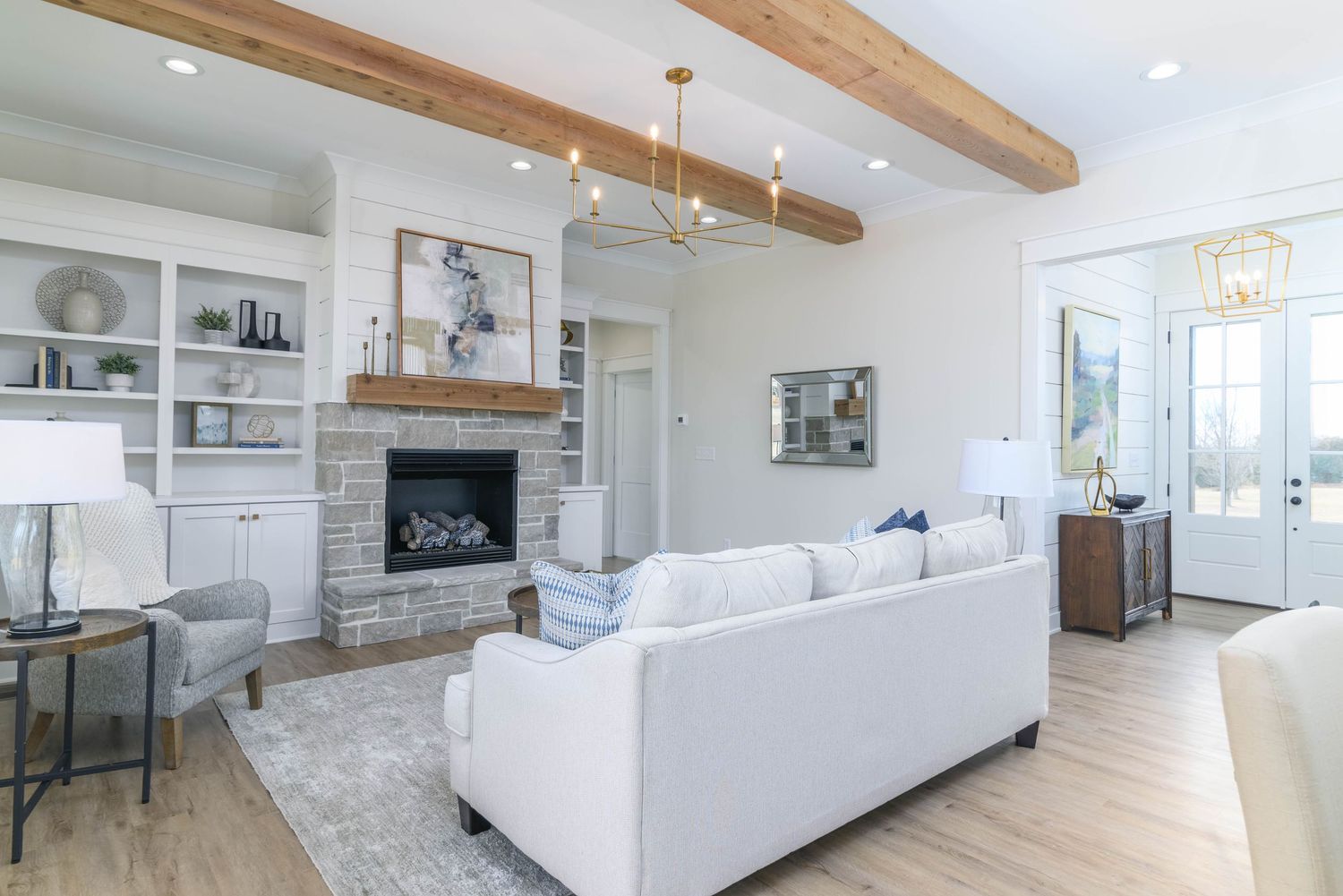 Bright living room with exposed wood beams, stone fireplace, built-in shelving, and white sofa.
