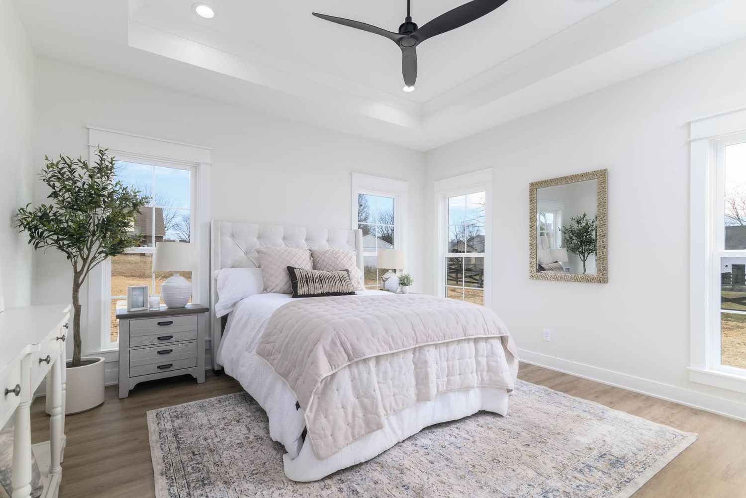 Spacious master bedroom with tray ceiling, ceiling fan, upholstered headboard, and hardwood floors.