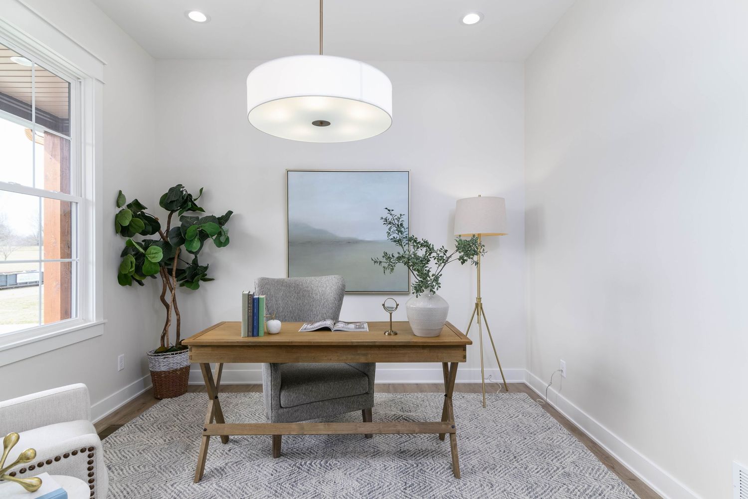 Minimalist home office with wooden desk, fiddle leaf fig plant, and neutral gray area rug.