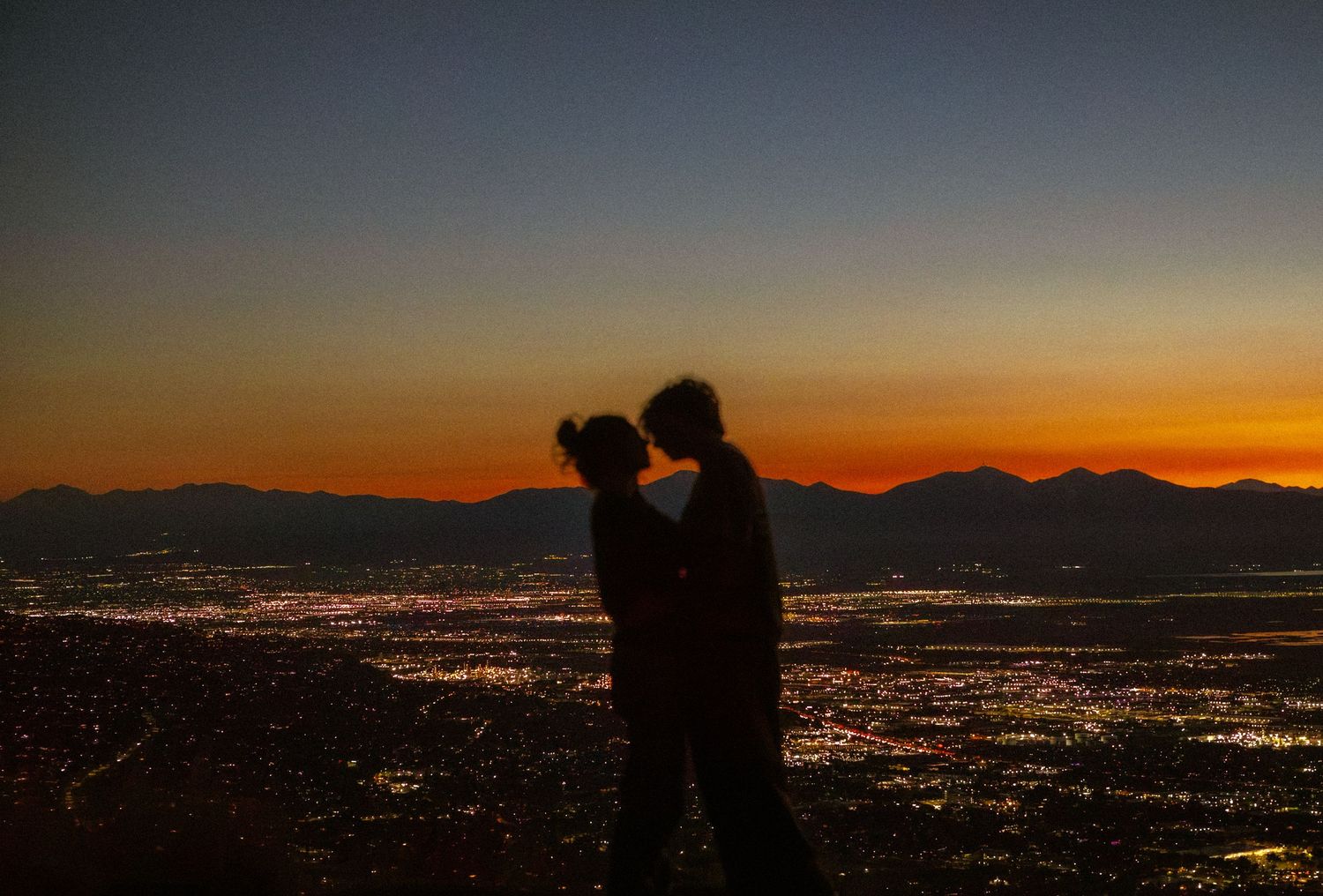 couple embraces in utah overlooking mountains and city during sunset