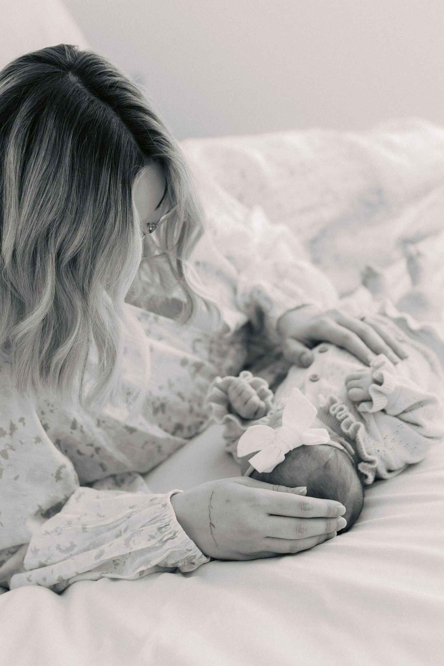 Black and white photo of a mother tenderly cradling her newborn baby while lying on a white bed.